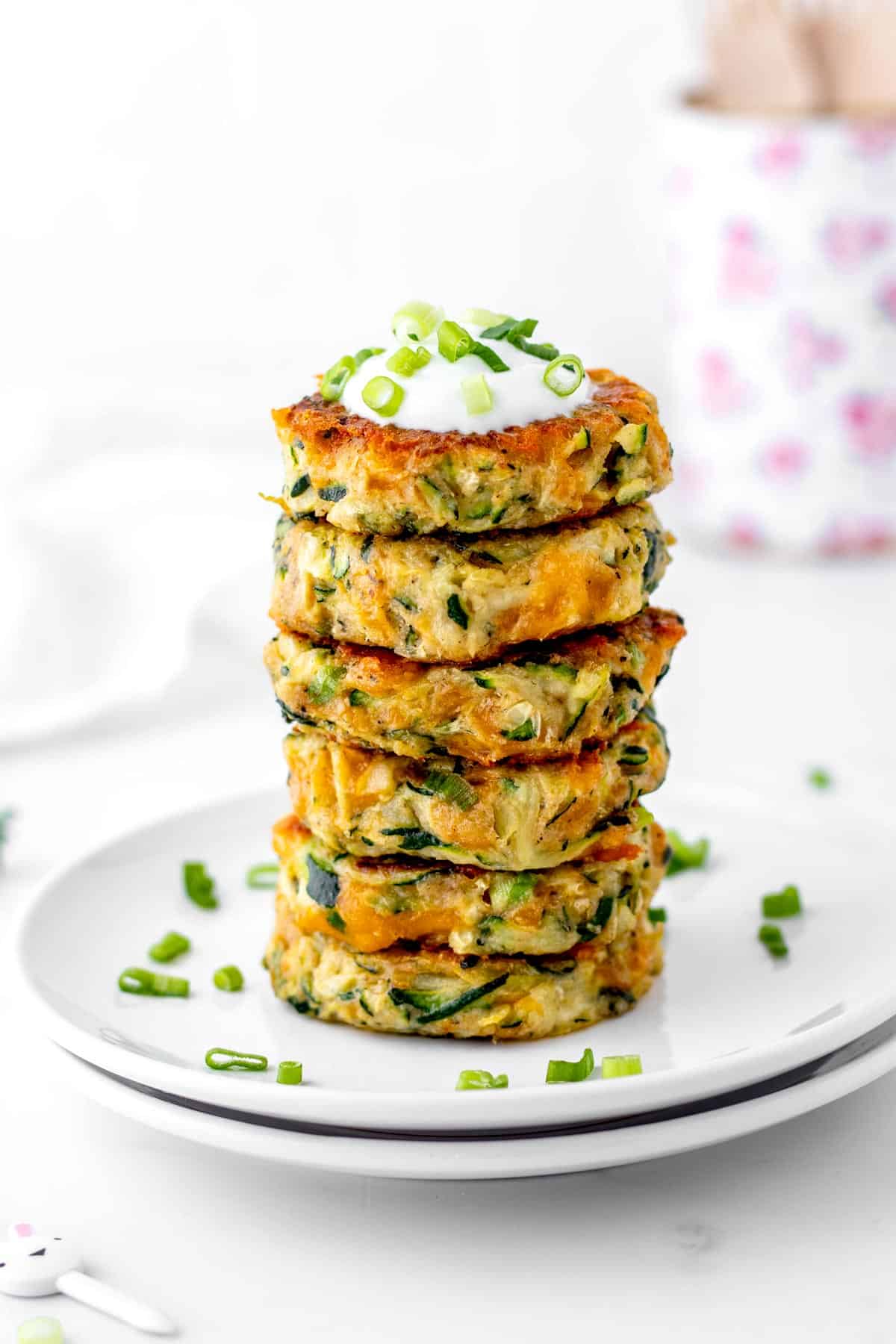 A stack of healthy zucchini fritters with some yogurt and green onions on top.
