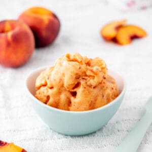 3 ingredient peach sorbet recipe in a small blue bowl with fresh peaches.
