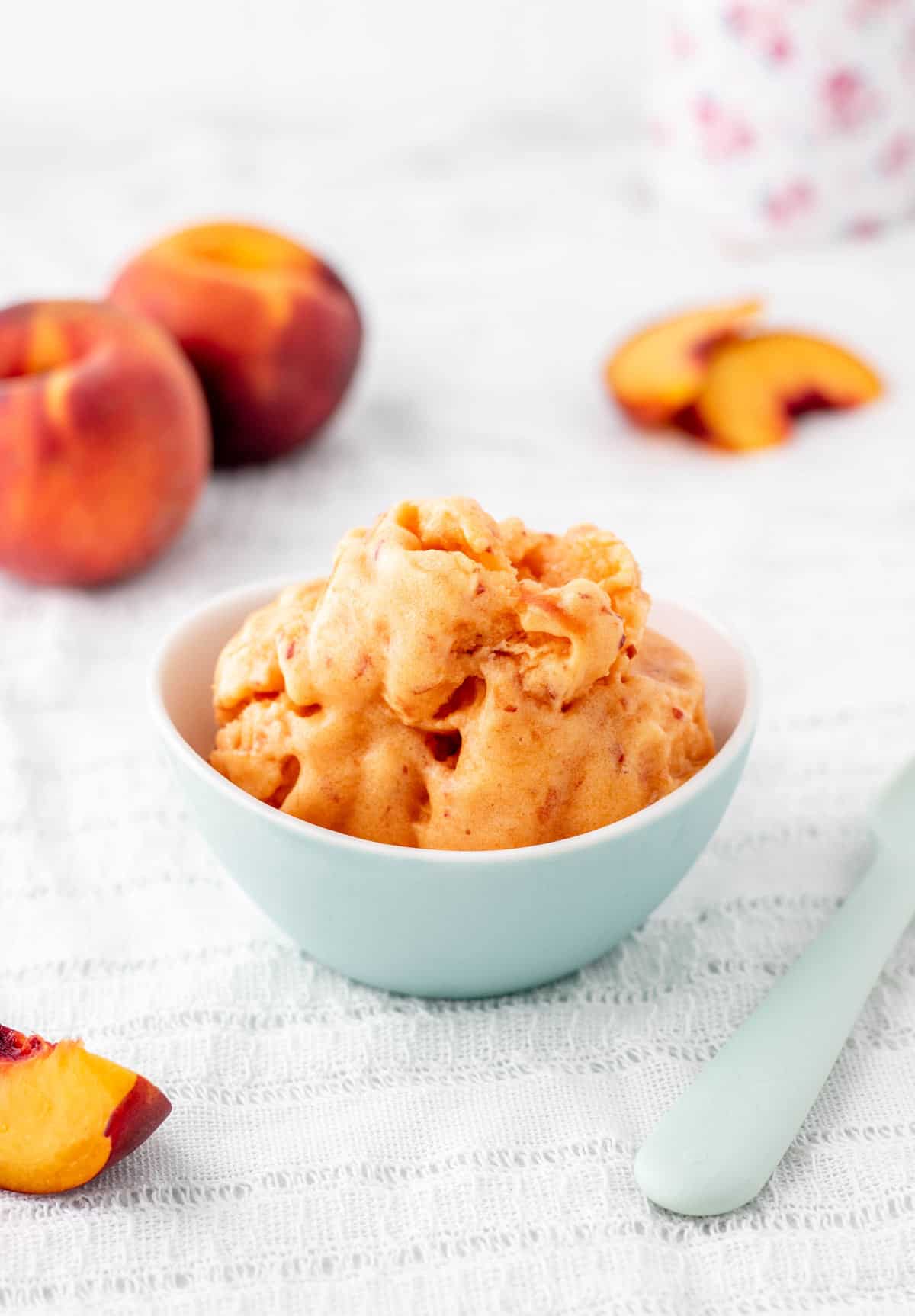 3 ingredient peach sorbet in a small bowl with fresh peaches.