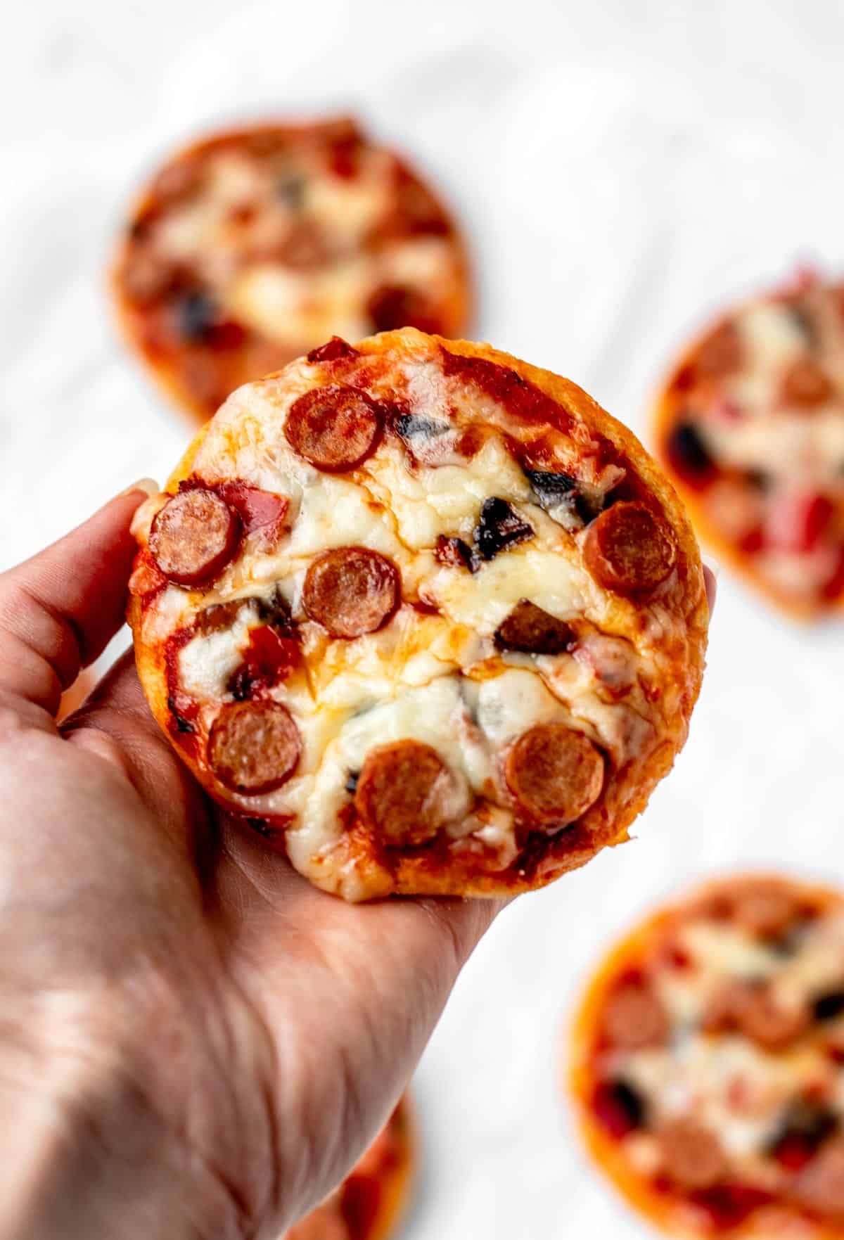 A hand holding up a mini pizza made with 3 ingredient pizza dough with no yeast.