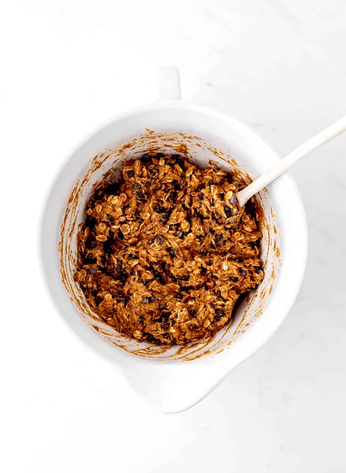 Chocolate chips added into the banana pumpkin mixture in a white bowl.