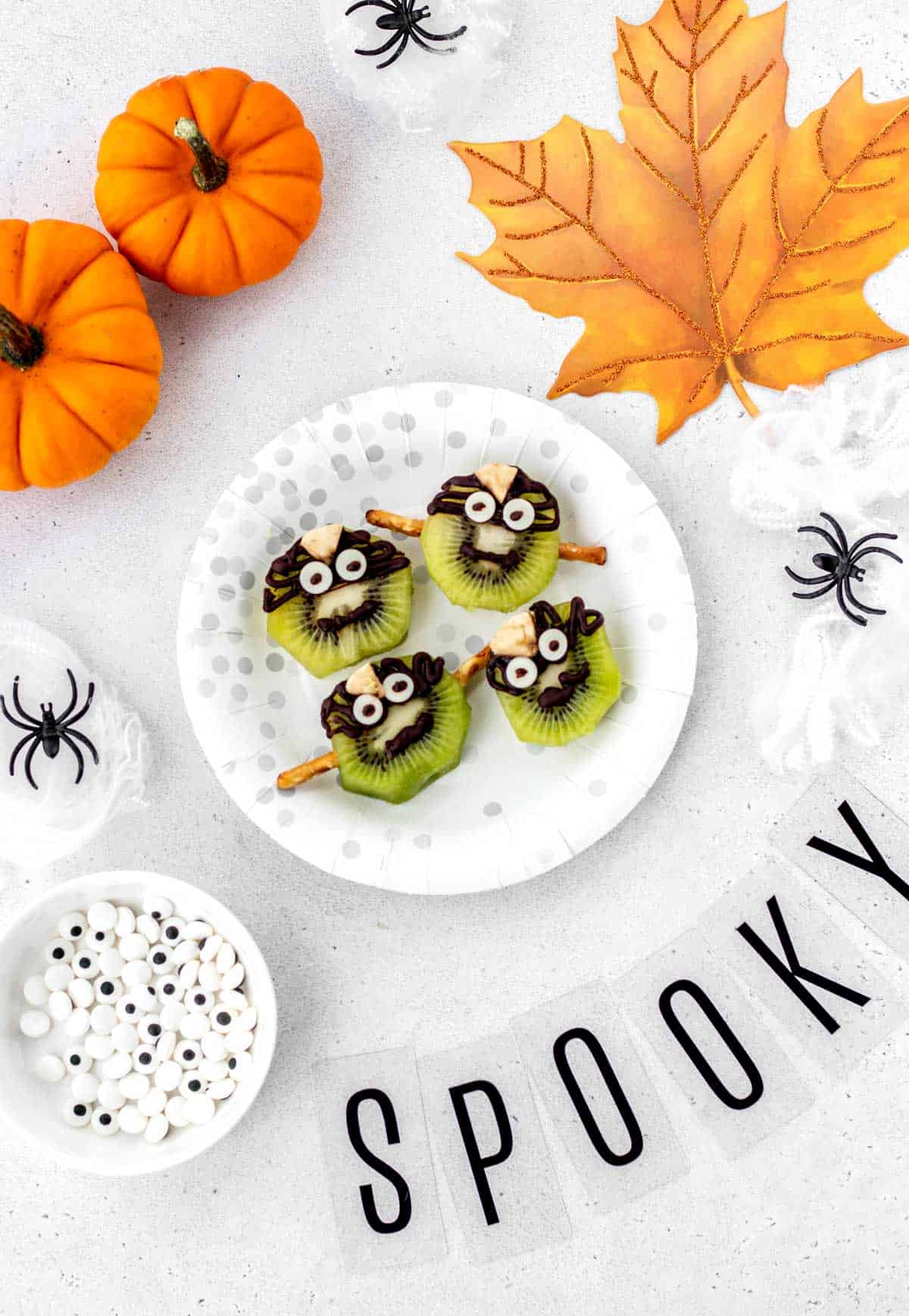 Four Frankenstein kiwis on a plate with Halloween decorations.