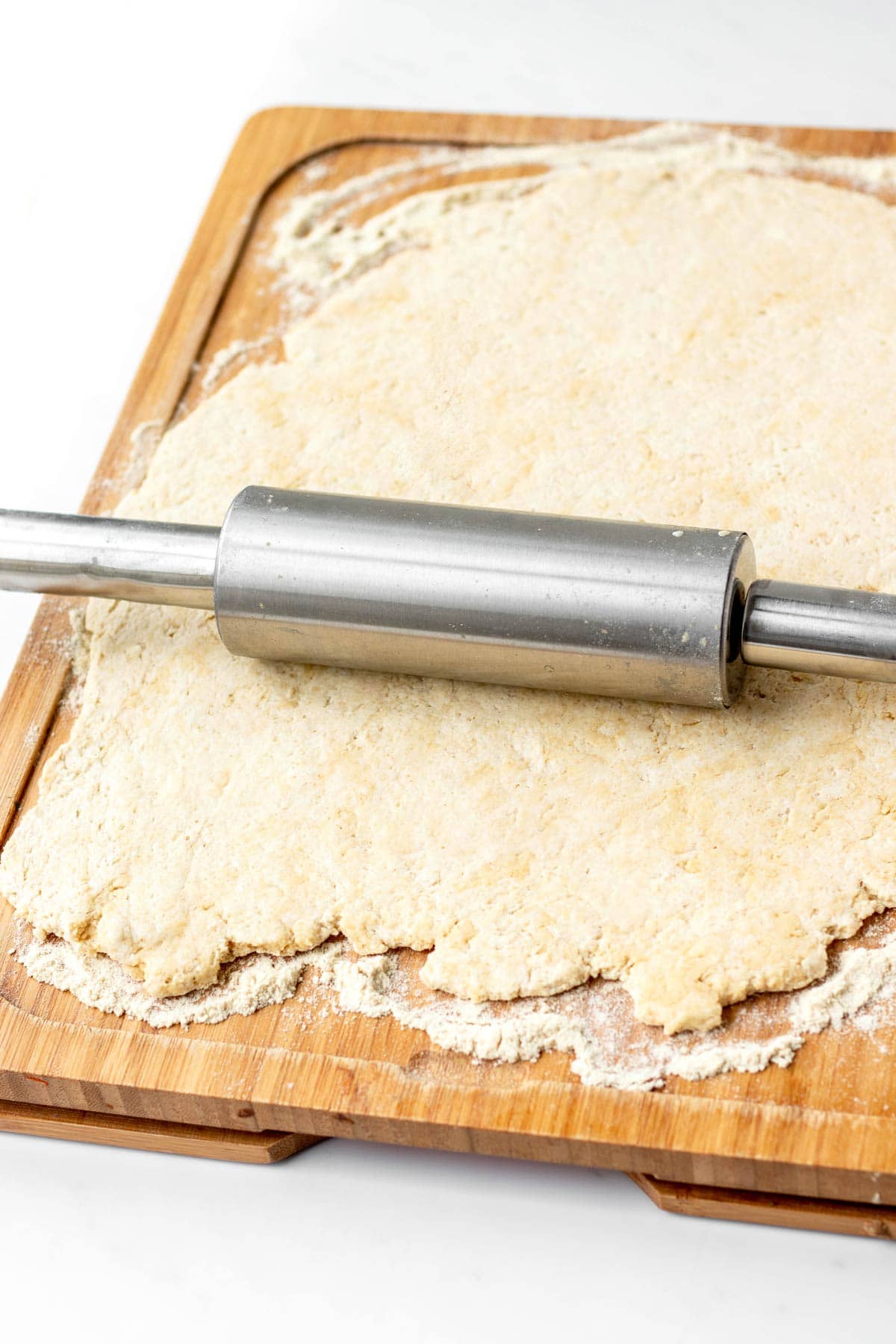 A rolling pin rolling out 3 ingredient pizza dough on a cutting board.
