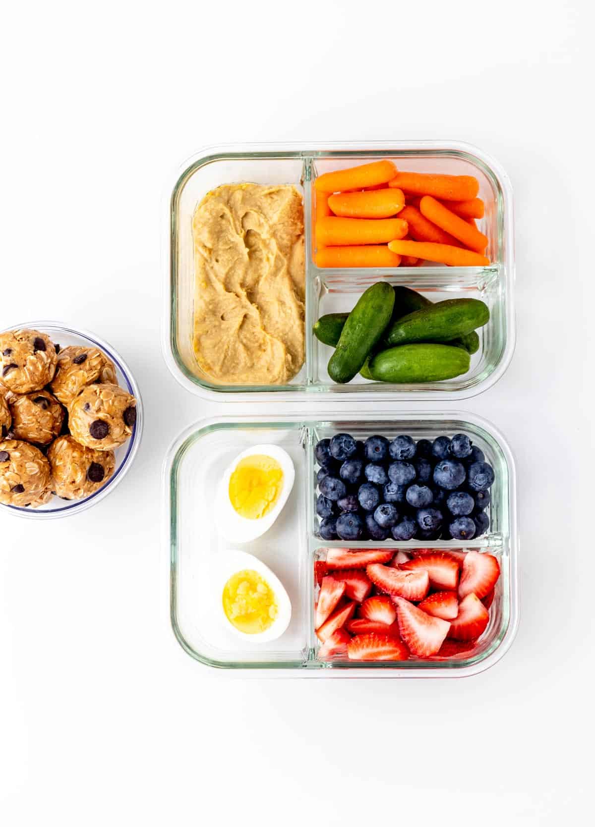Healthy travel snacks including fruits, veggies, hummus, hard boiled eggs and energy balls packed in containers.