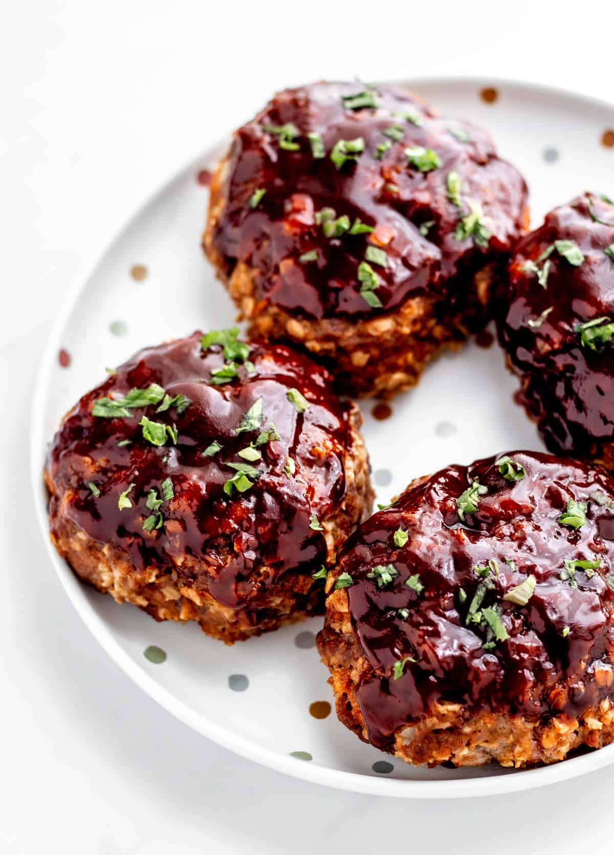 A plate with four mini meatloaves topped with glaze and parsley.