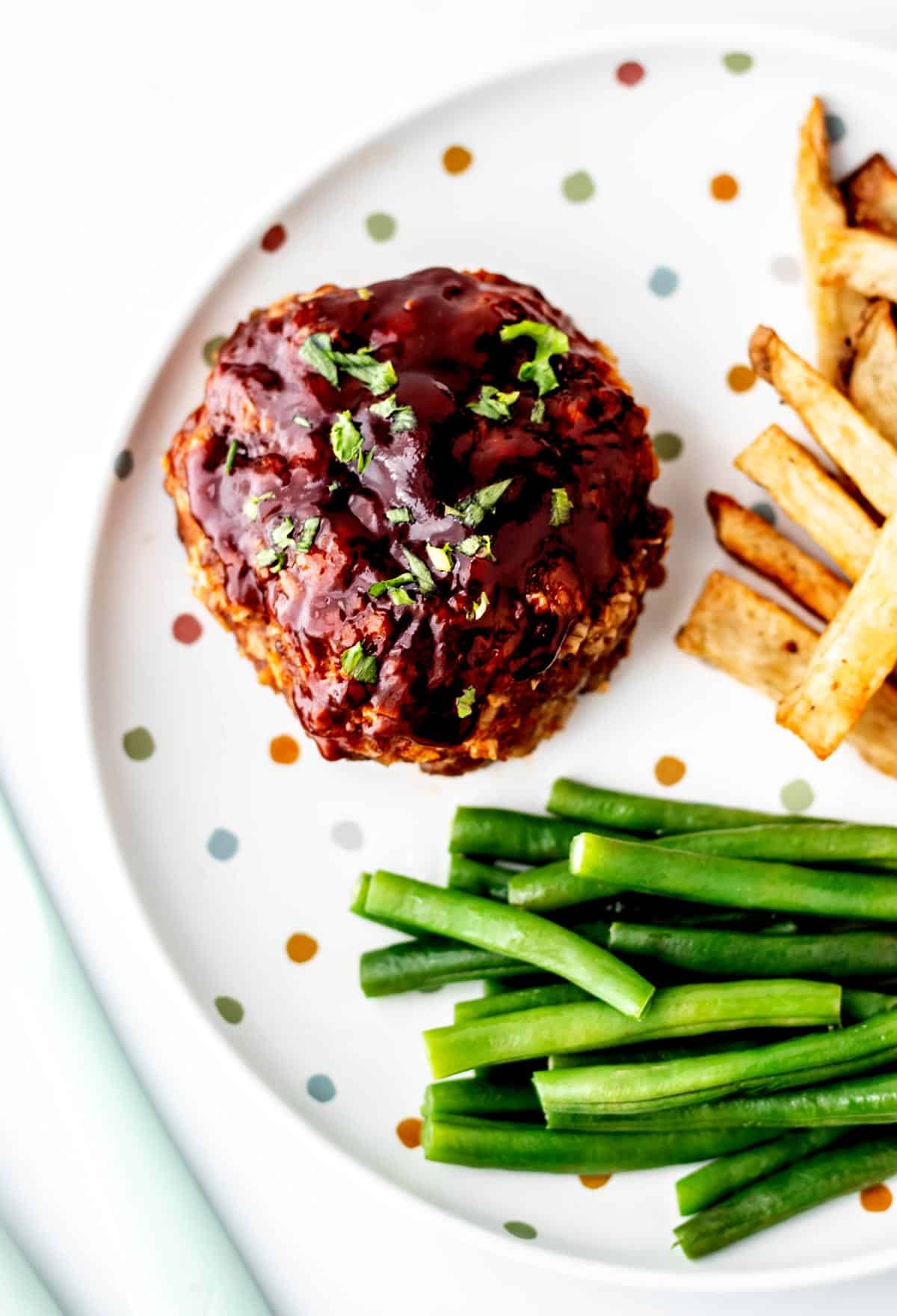 Close up image of mini meatloaf on a plate with green beans and homemade fries.