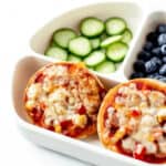 Two air fryer mini pizzas in a divided plate with cucumbers and blueberries.