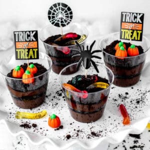 Four Halloween dirt cups on a white tray with gummy worms and candy pumpkins.