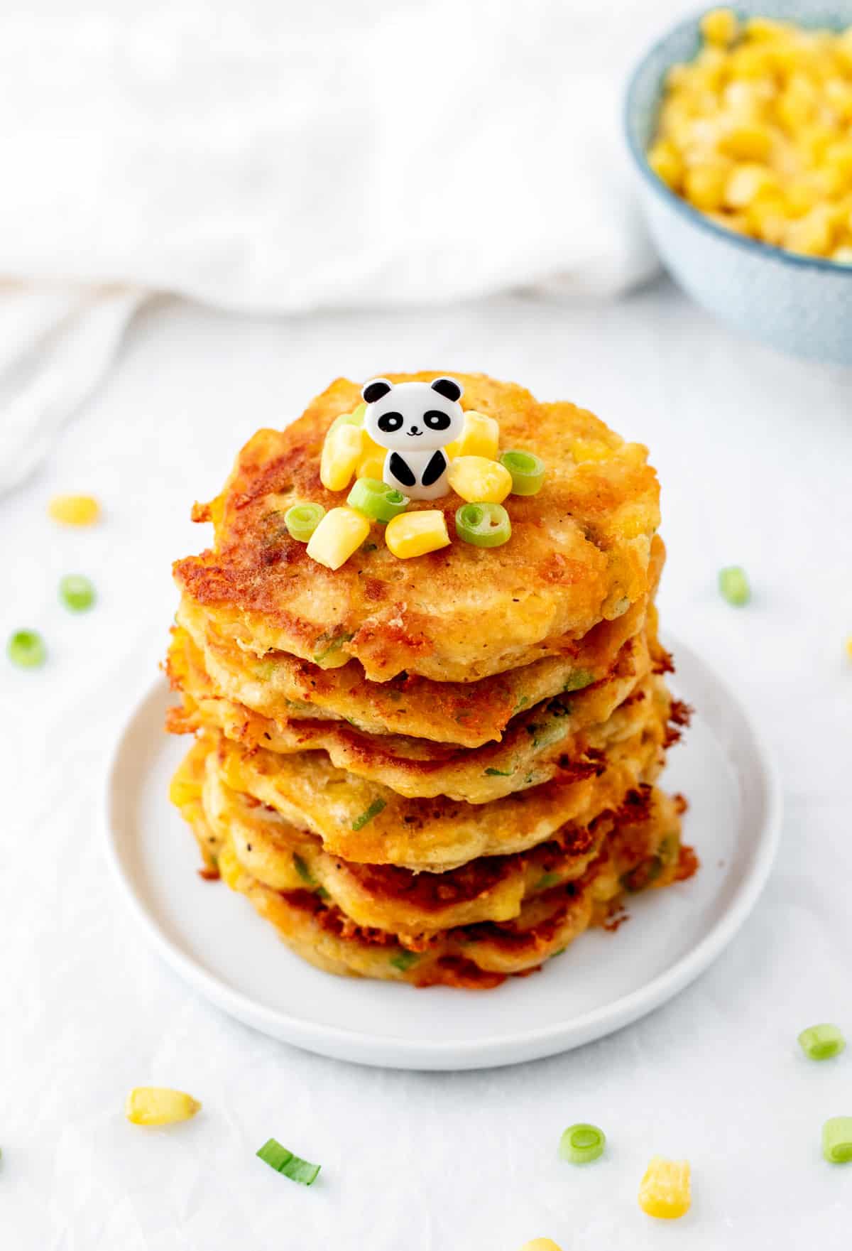 A stack of healthy corn fritters on a plate topped with corn kernels and green onion.