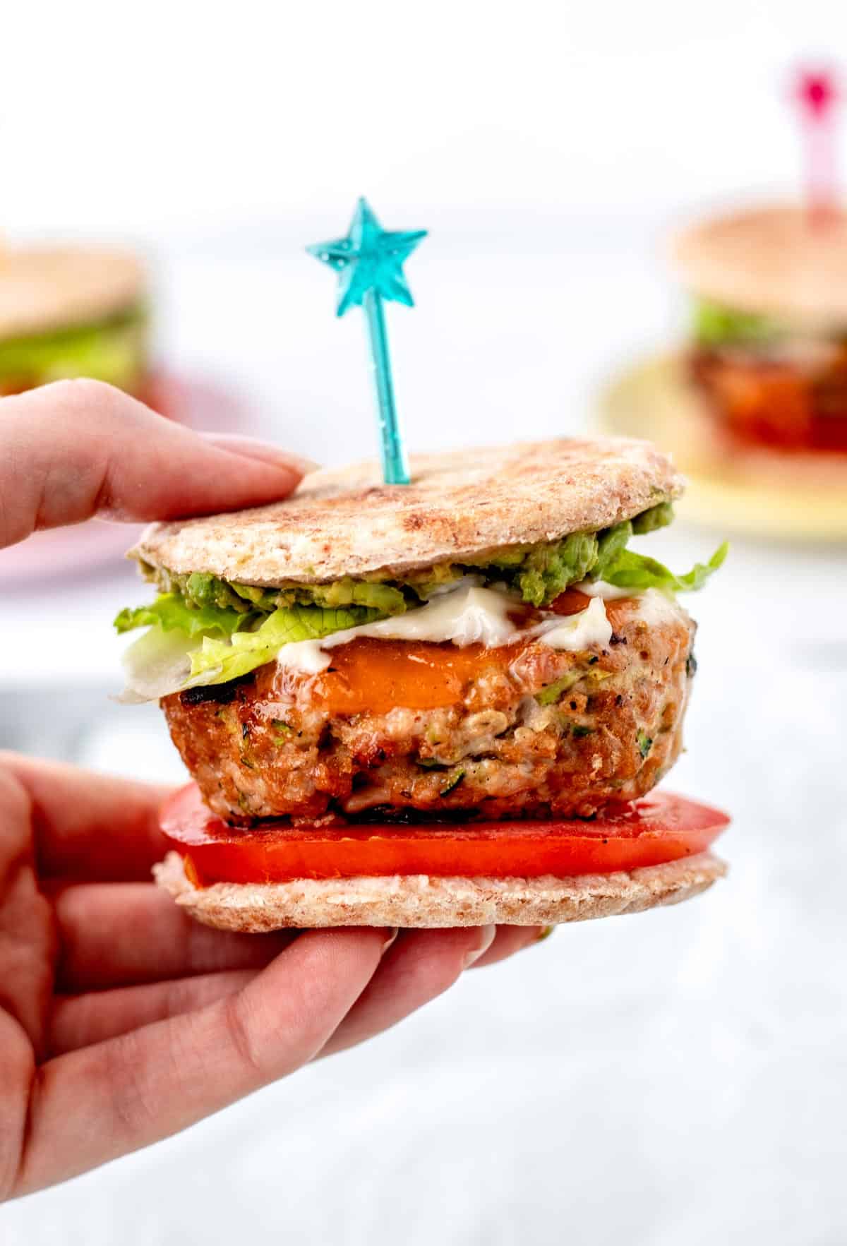 A hand holding up a juicy turkey slider with toppings.