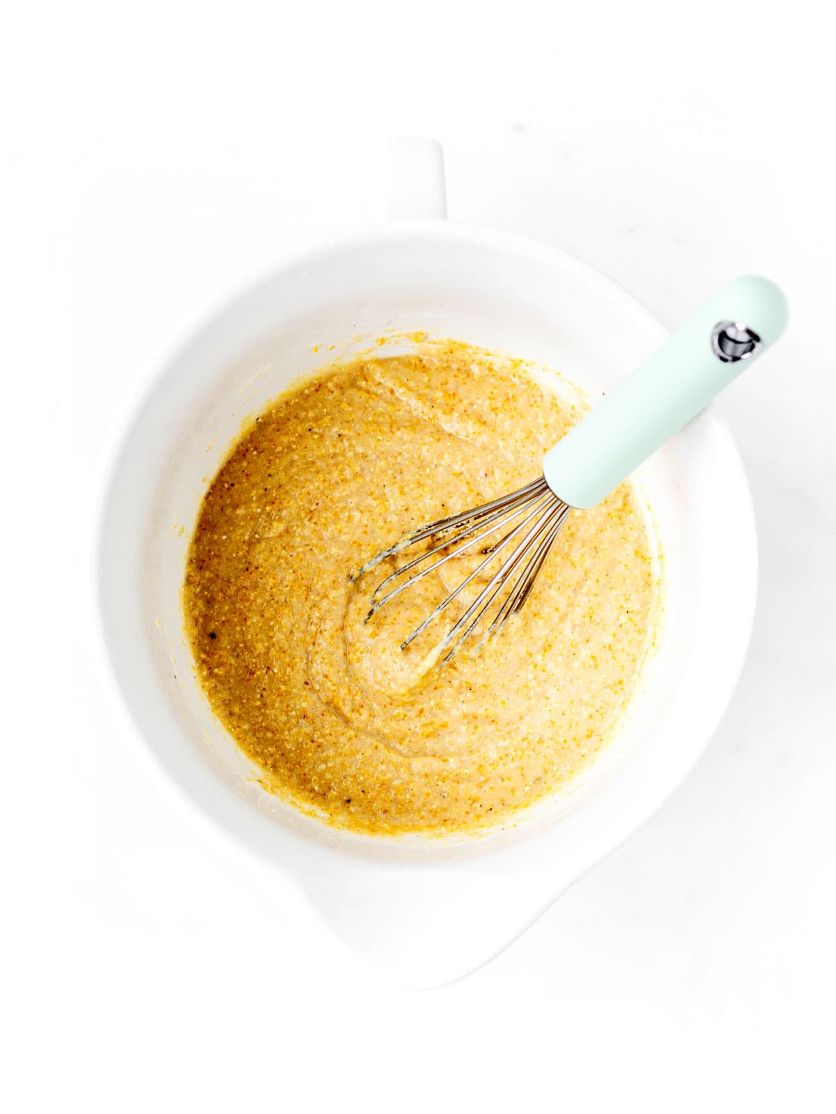 The cornbread muffin batter being whisked together in a white bowl.
