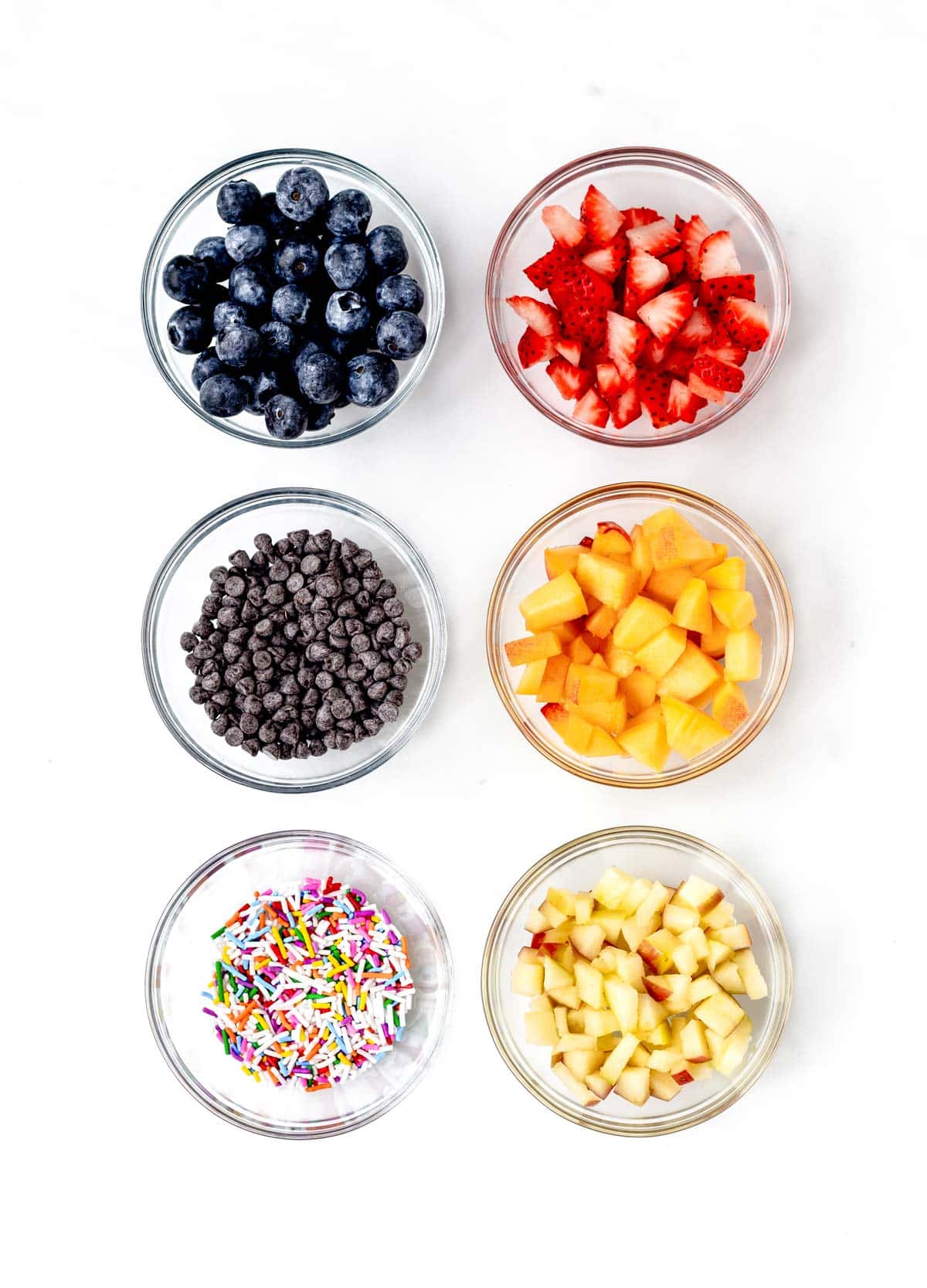 Different toppings in six bowls for pancake donuts.