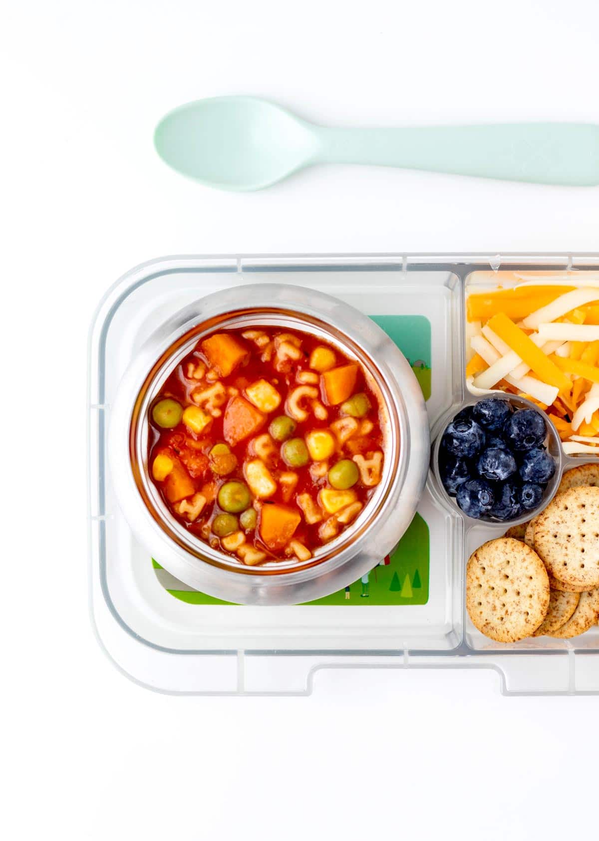 Veggie noodle soup in a thermos in a lunchbox with cheese, crackers and blueberries.