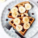 3-ingredient banana waffles on a blue plate with banana slices, chocolate chips and a fork.