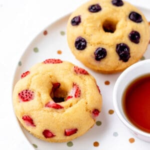 Two pancake donuts on a plate topped with berries.