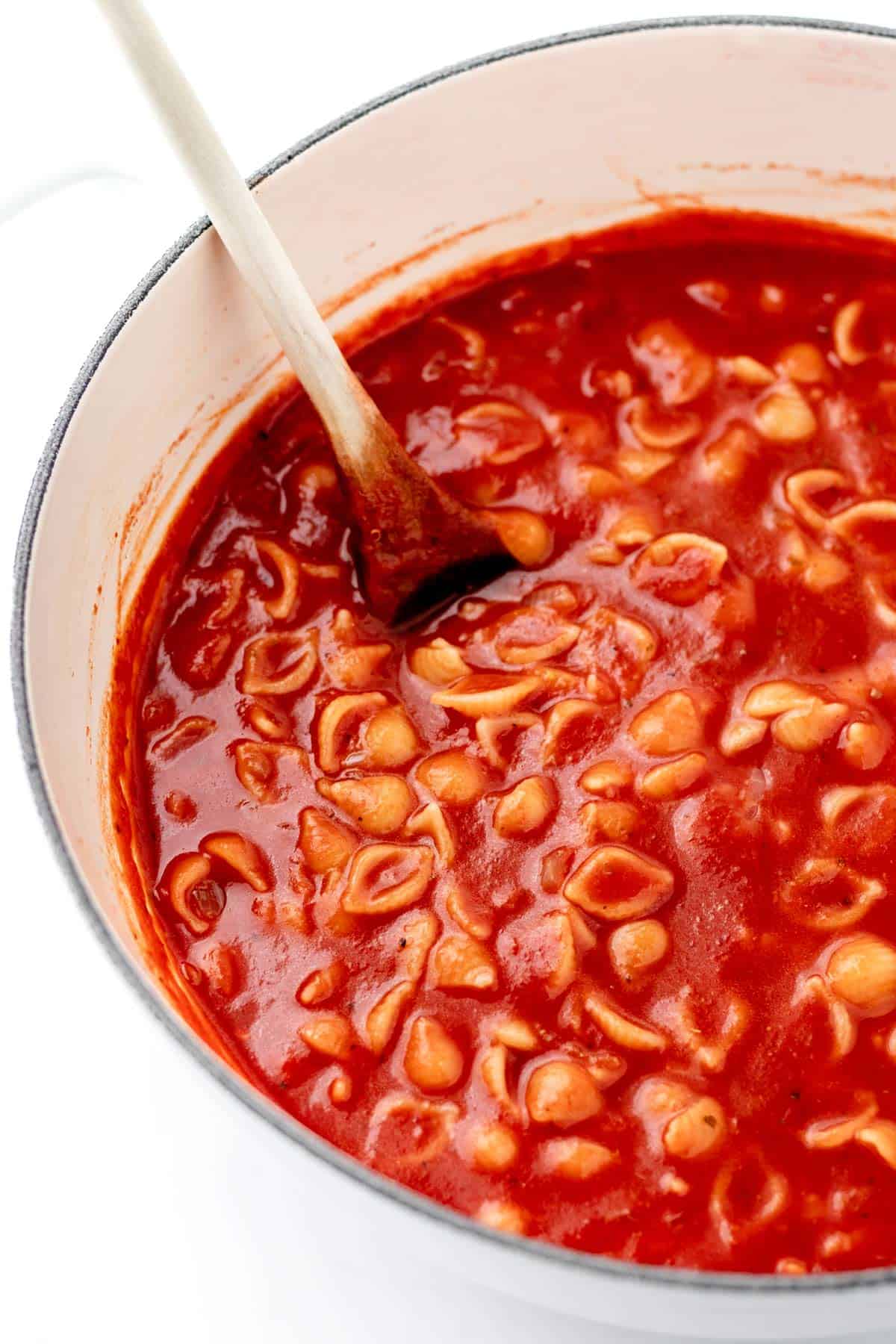 A close up image of a large pot full of noodles and red sauce with a spoon.