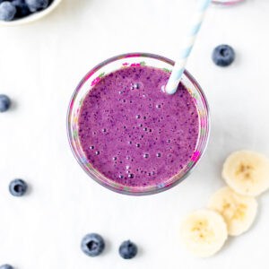 Overhead image of mixed berry and banana smoothie in a cup with a blue straw.