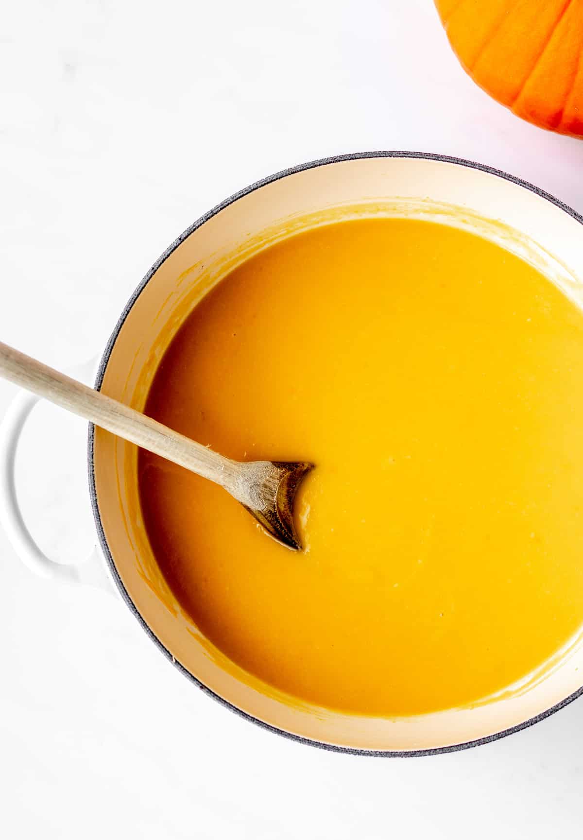 A large pot of pumpkin soup with a wooden spoon.