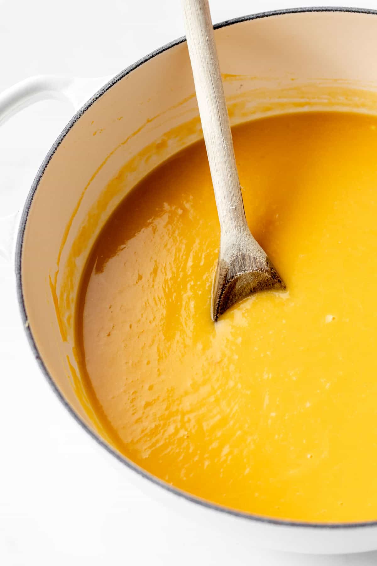 Pumpkin soup with coconut milk in a large pot with a wooden spoon.
