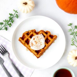 A pumpkin oat waffle topped with yogurt on a white plate with fork and knife.
