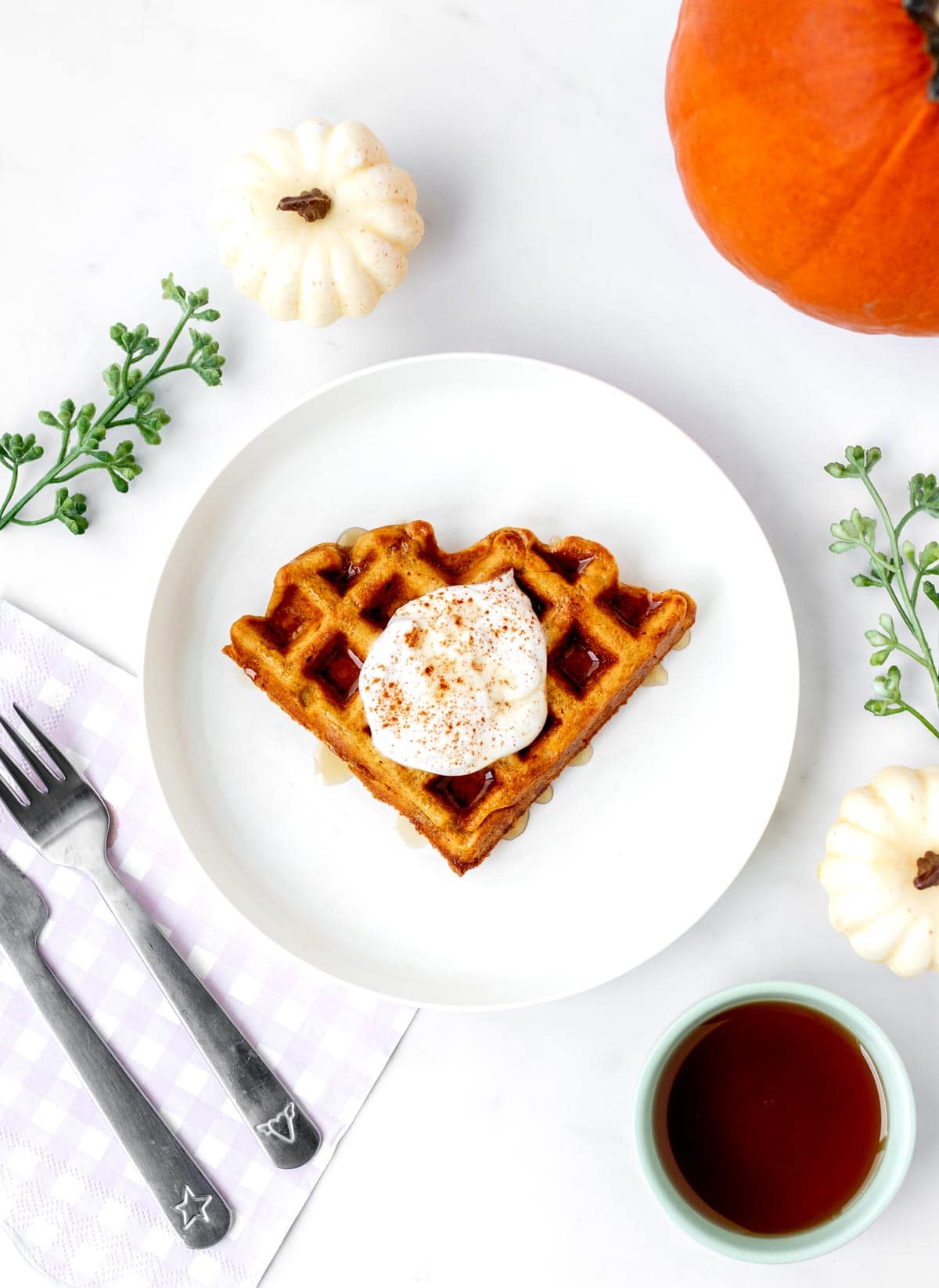 A white plate with a pumpkin oat waffle with yogurt on top with fall decor around the plate.
