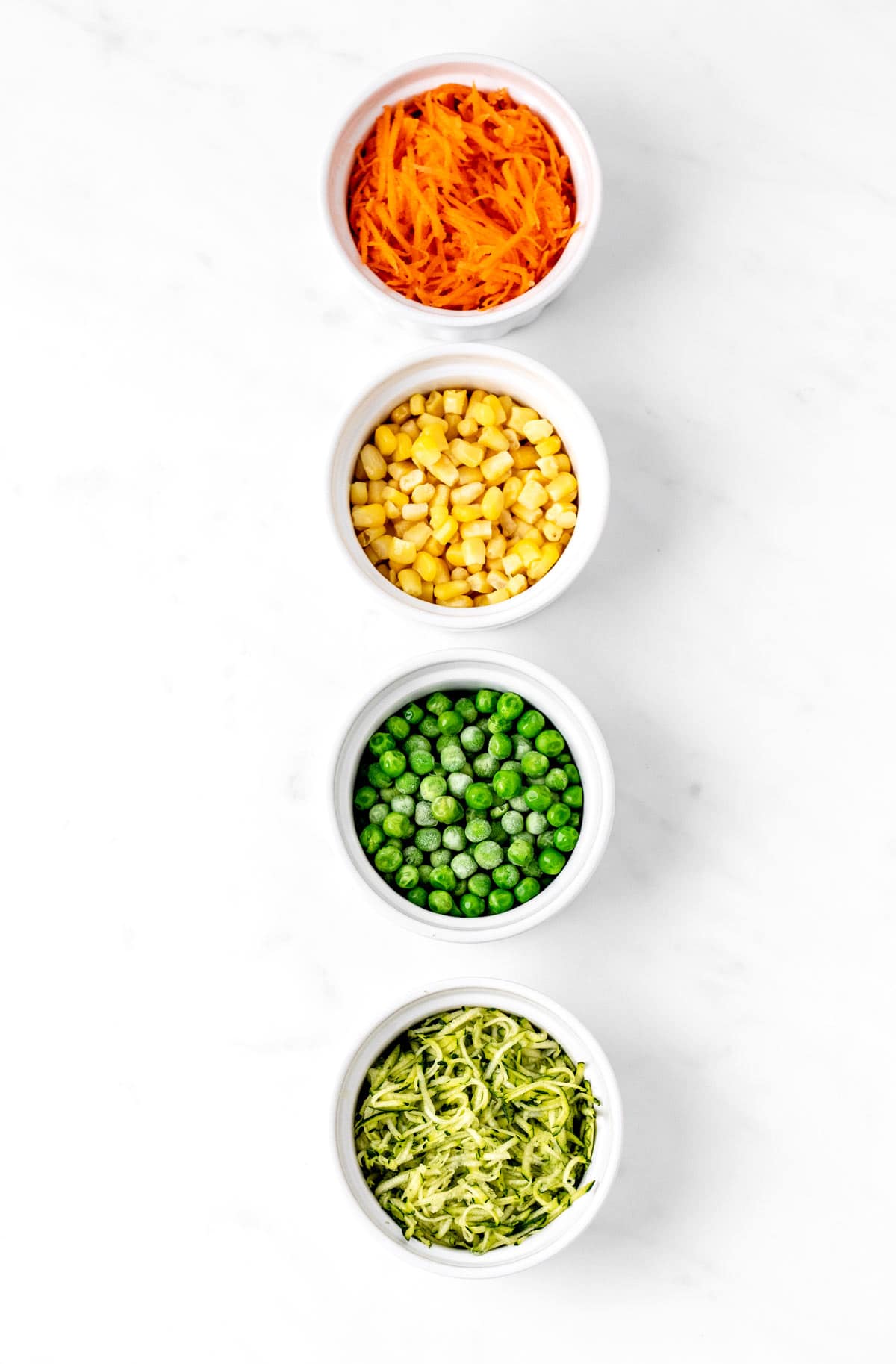 Carrots, corn, peas and zucchini in four small bowls.