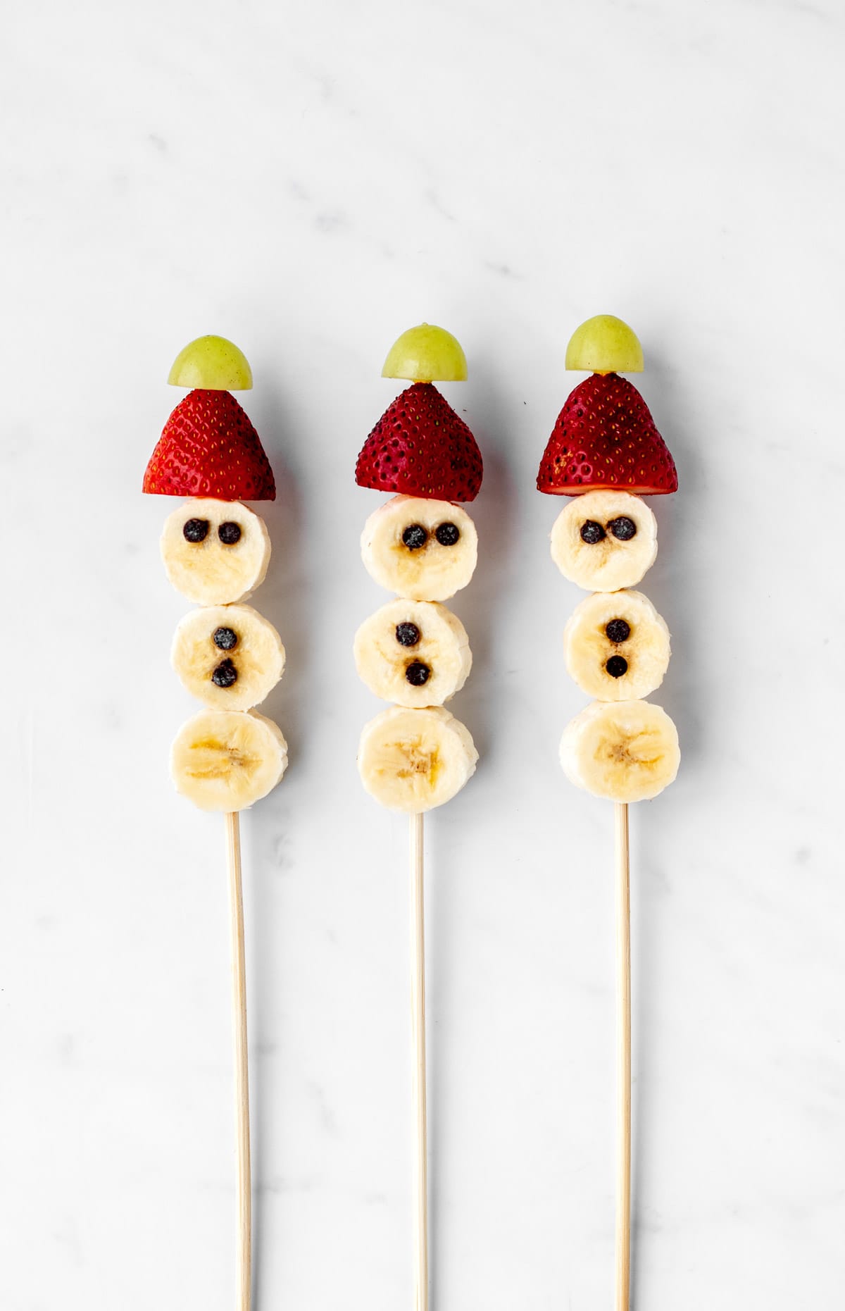 Banana snowmen on three sticks with chocolate chips eyes and buttons added.