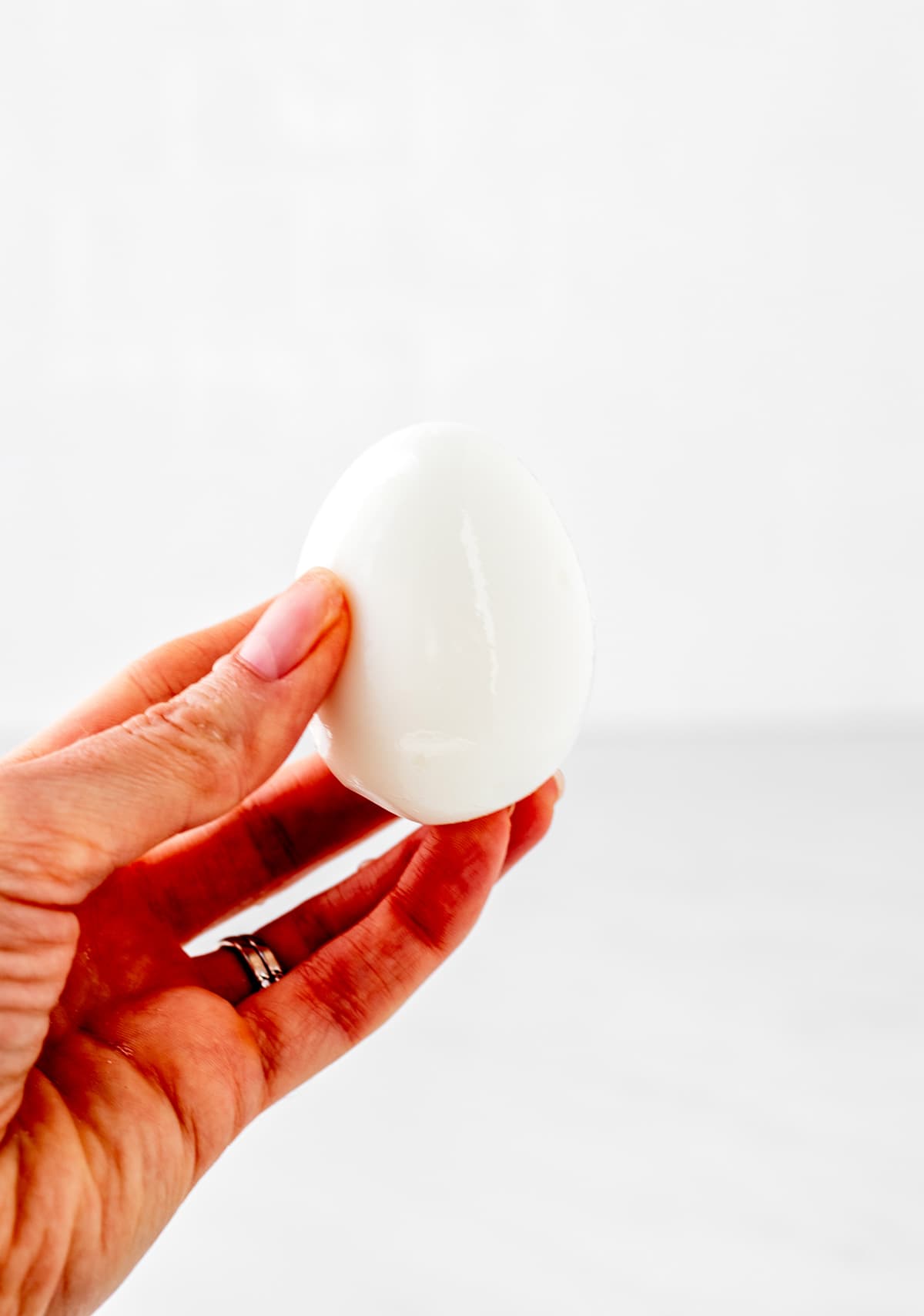 A hand holding up a cooked and peeled hard boiled egg.