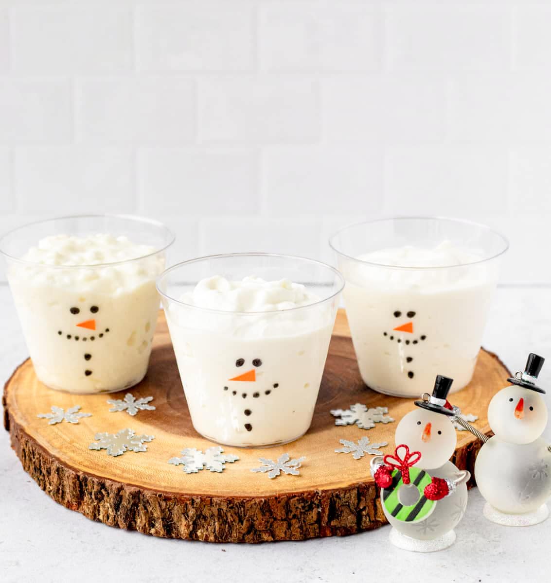 Three frosty yogurt cups on a wooden platter, with decorative snowflakes scatted on the platter.
