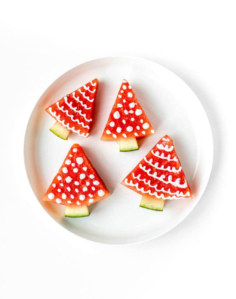 Four decorated watermelon Christmas trees on a white plate.