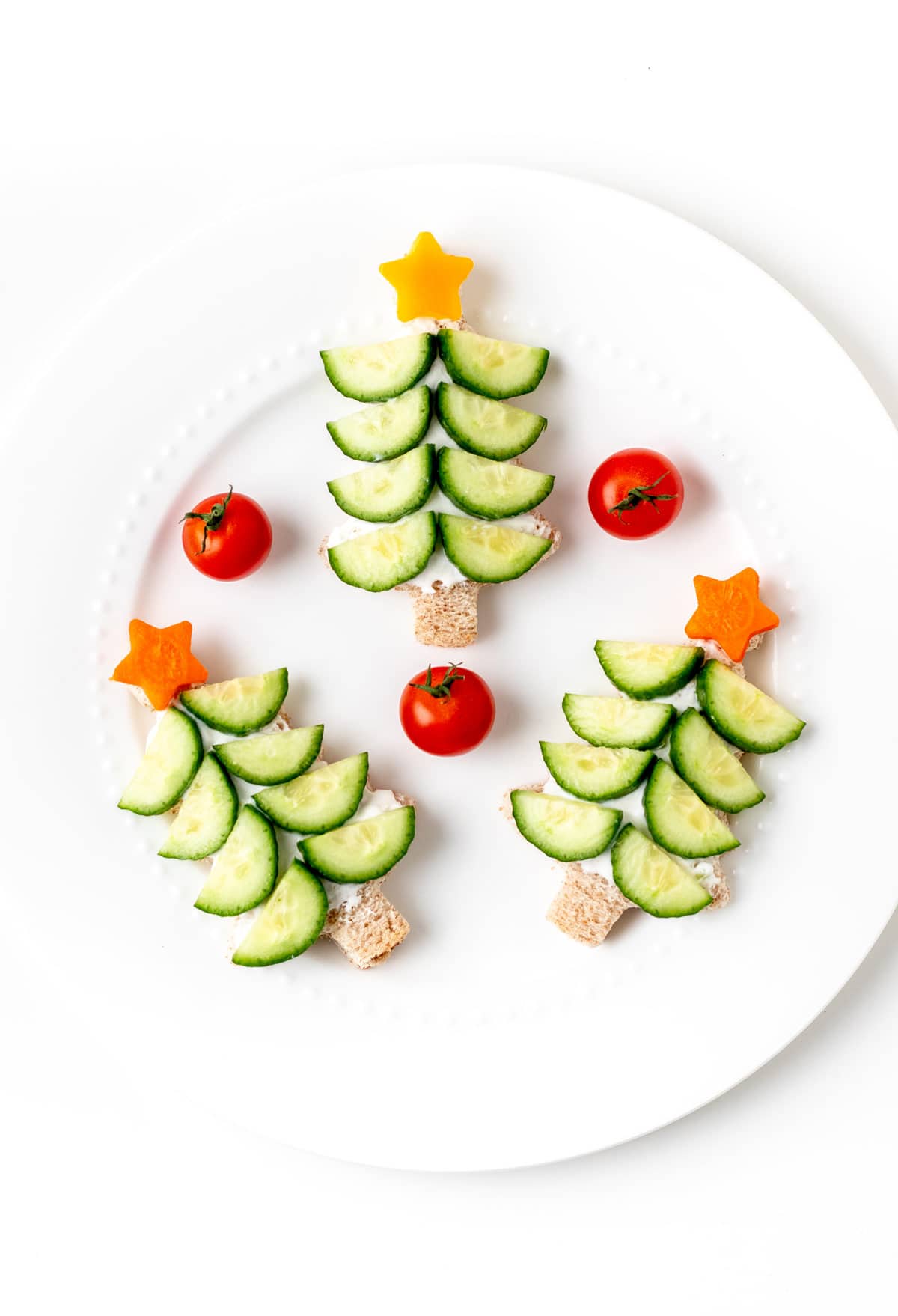 Three cucumber Christmas tree sandwiches on a plate with cherry tomatoes.