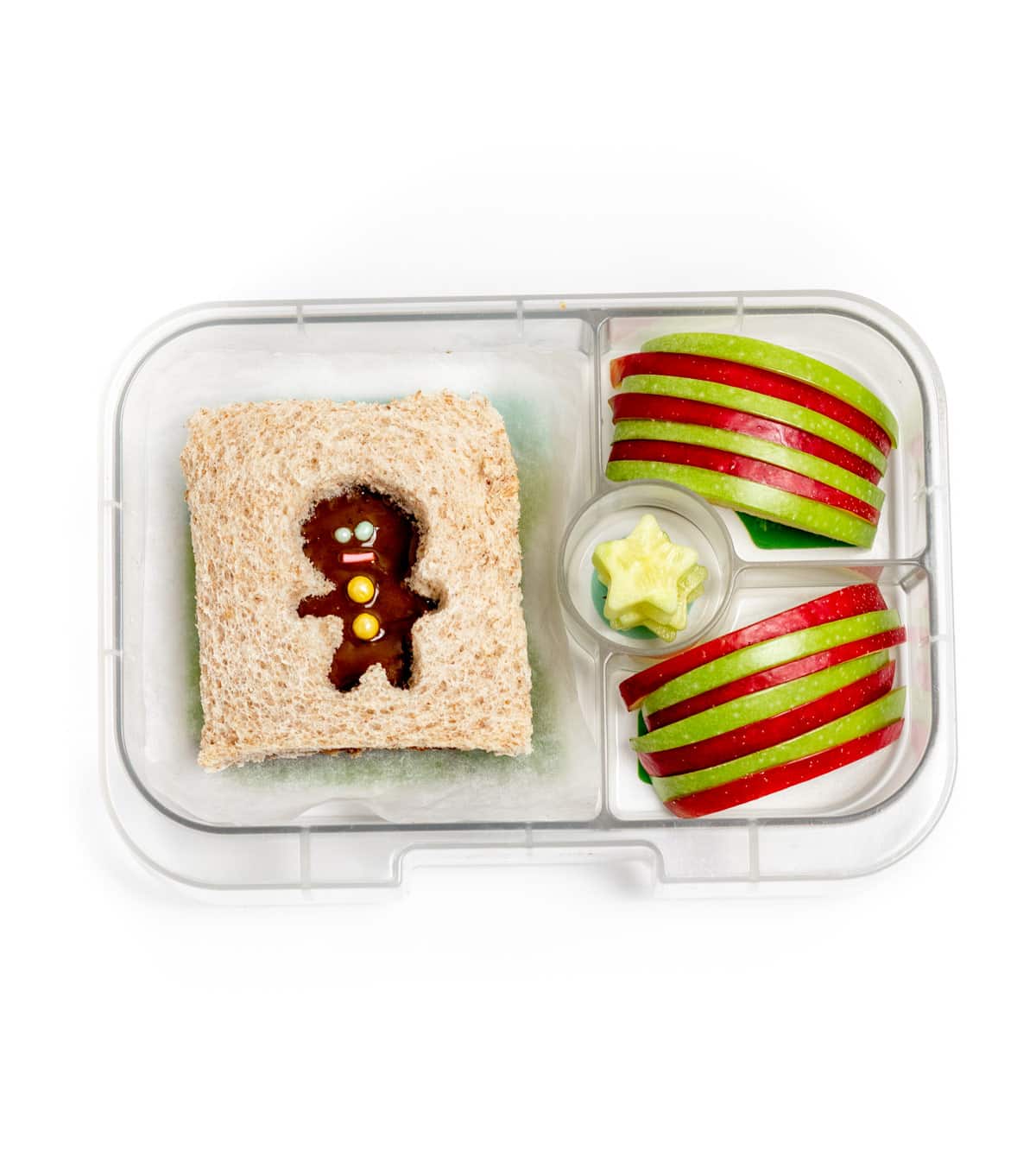 A lunchbox with one gingerbread man sandwich, cucumber slices cut into mini stars, and an arrangement of red and green apple slices.
