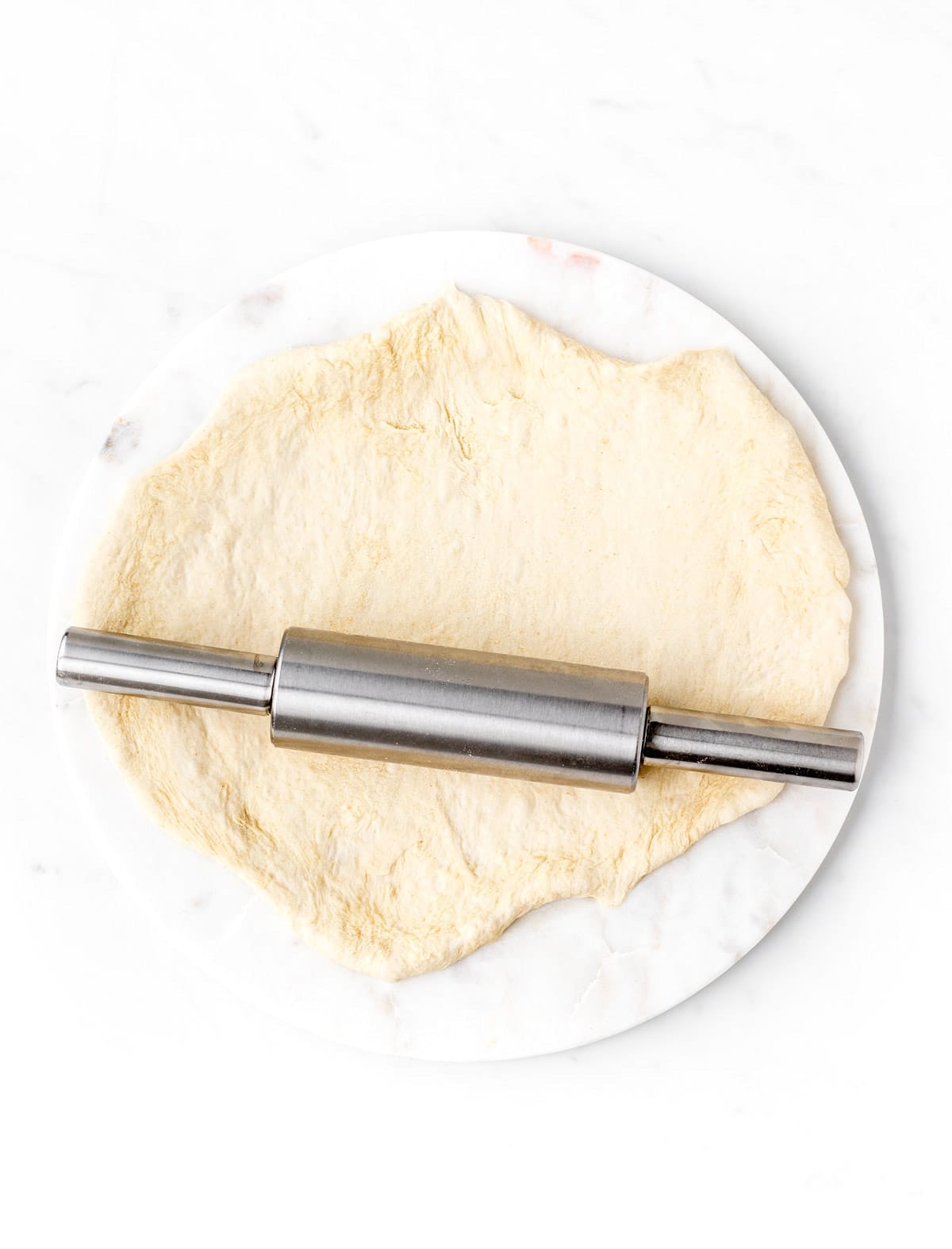 The pizza dough being rolled out and a plate with a rolling pin.