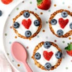Three granola yogurt cups with berries on a polka dot plate.