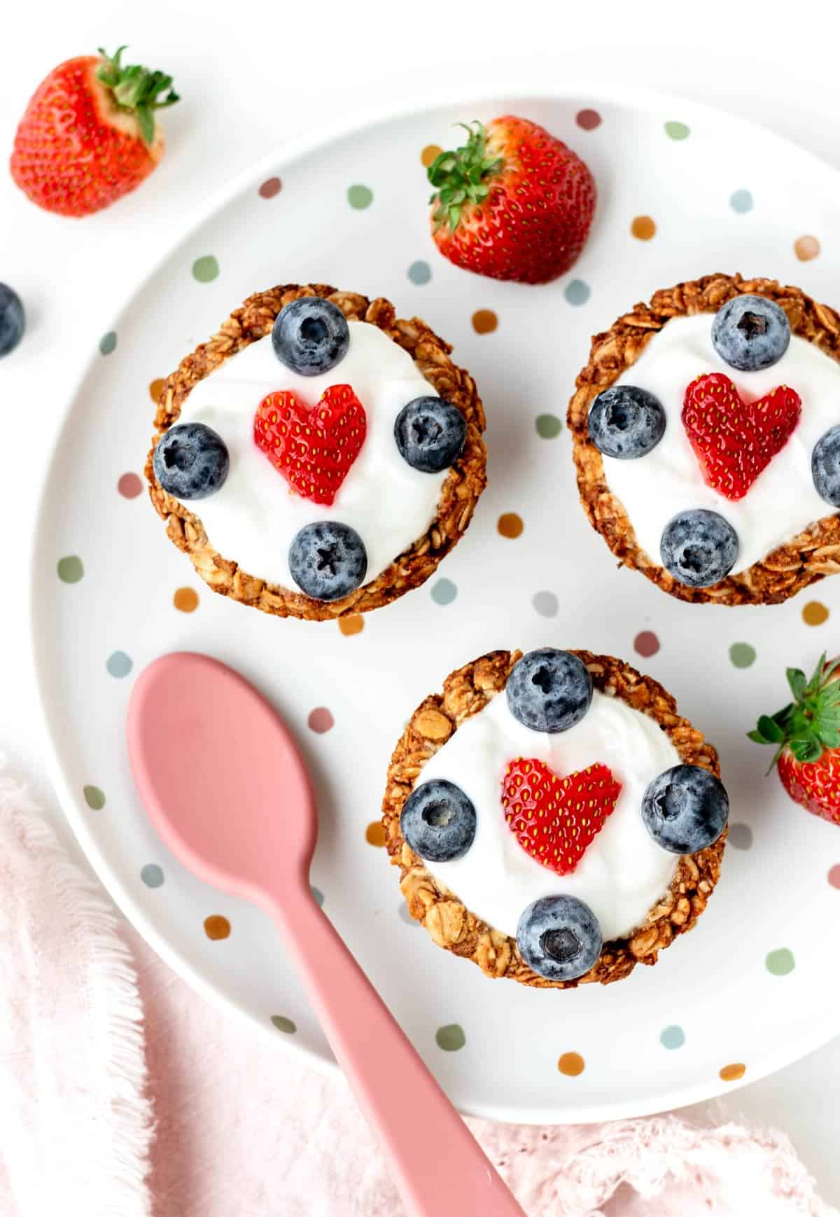 3 granola yogurt cups with berries on a polka dot decorative plate.