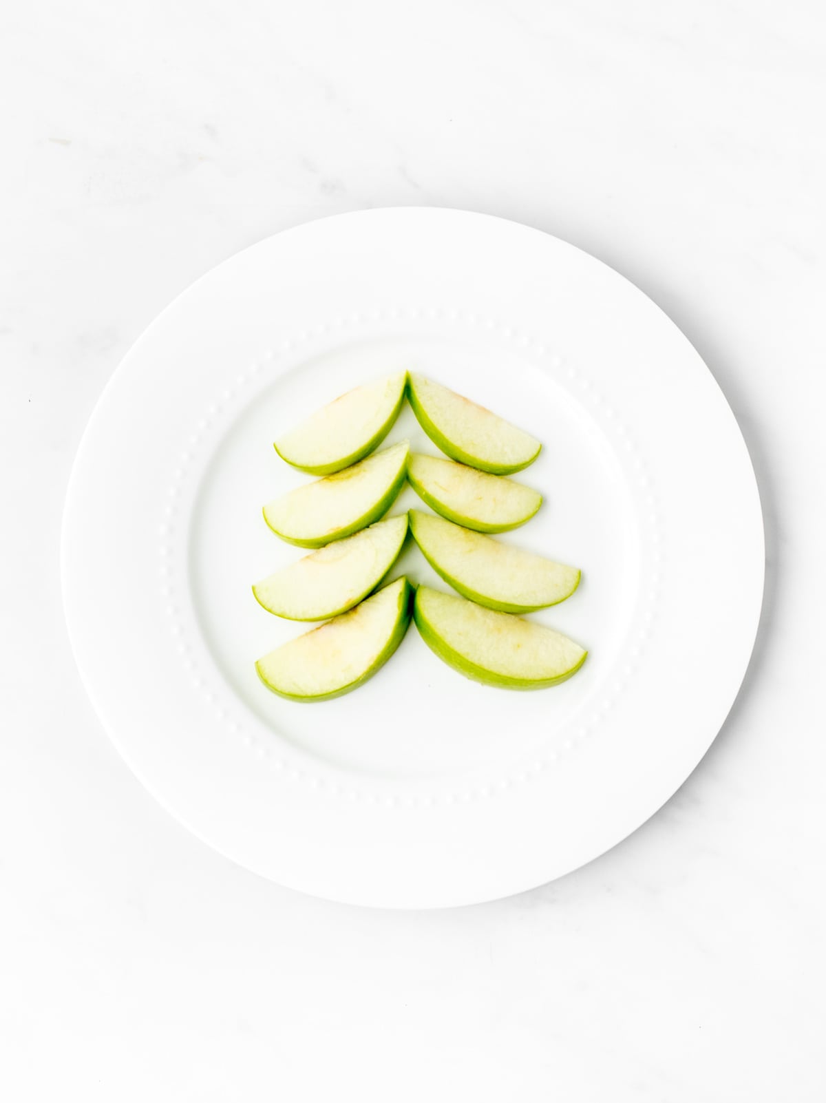 Apple slices on a white plate, spread out to look like a Christmas tree.