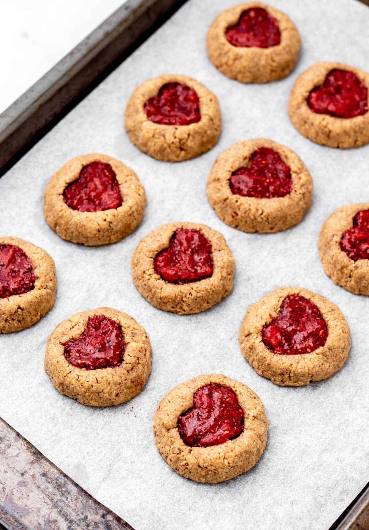 Heart thumbprint cookies on a cooking sheet lined with parchment paper, after coming out of the oven.