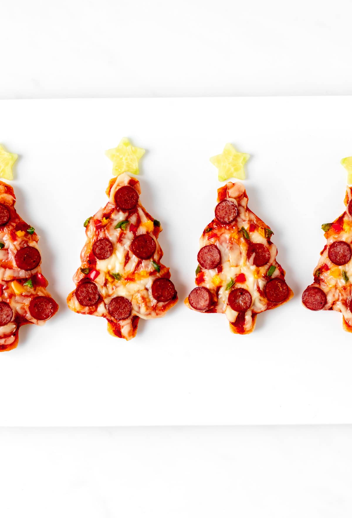 Multiple mini Christmas tree pizzas lined up side by side on a white tray.