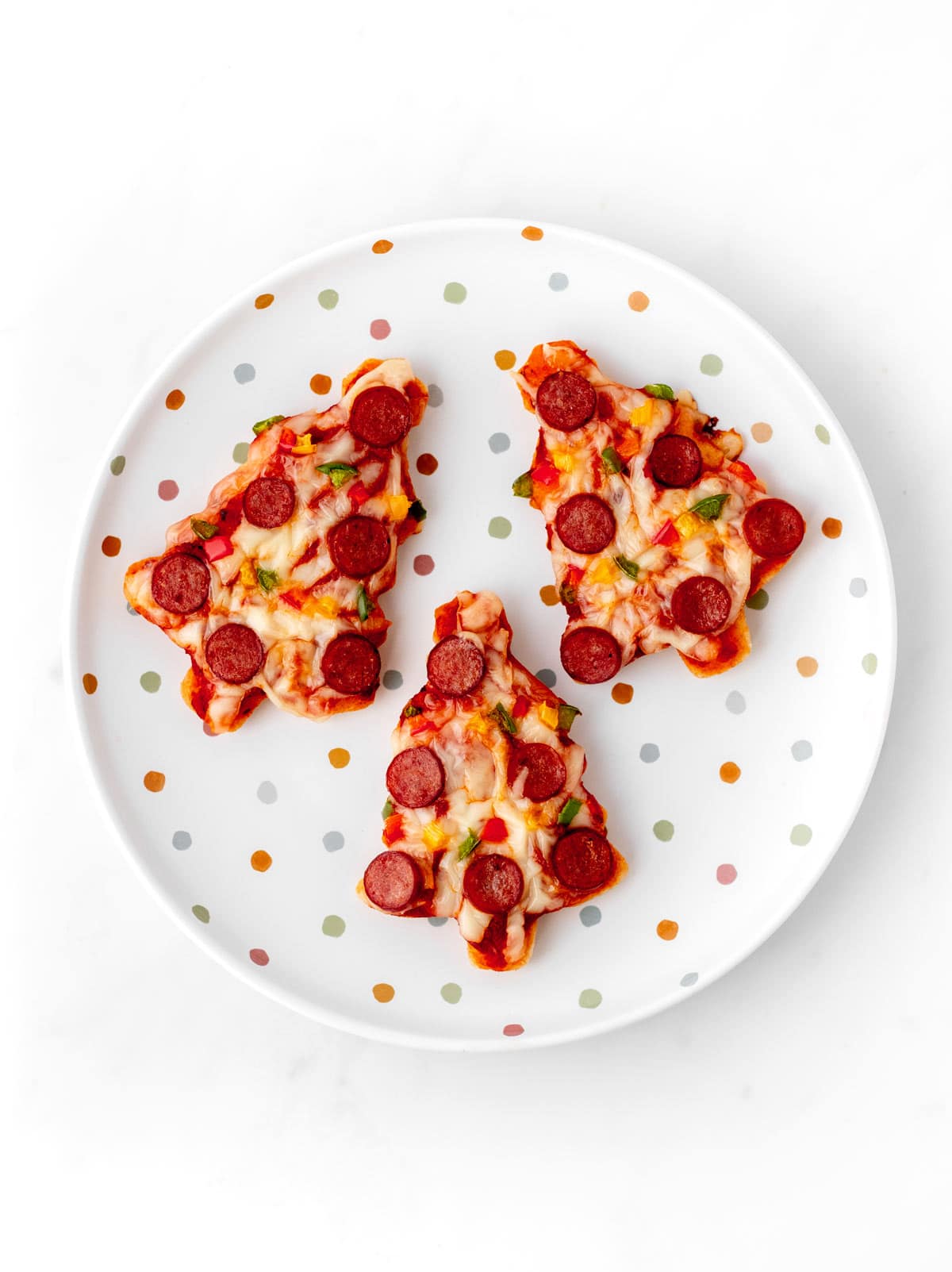 A birds-eye view of three mini Christmas tree pizzas on a decorative plate.