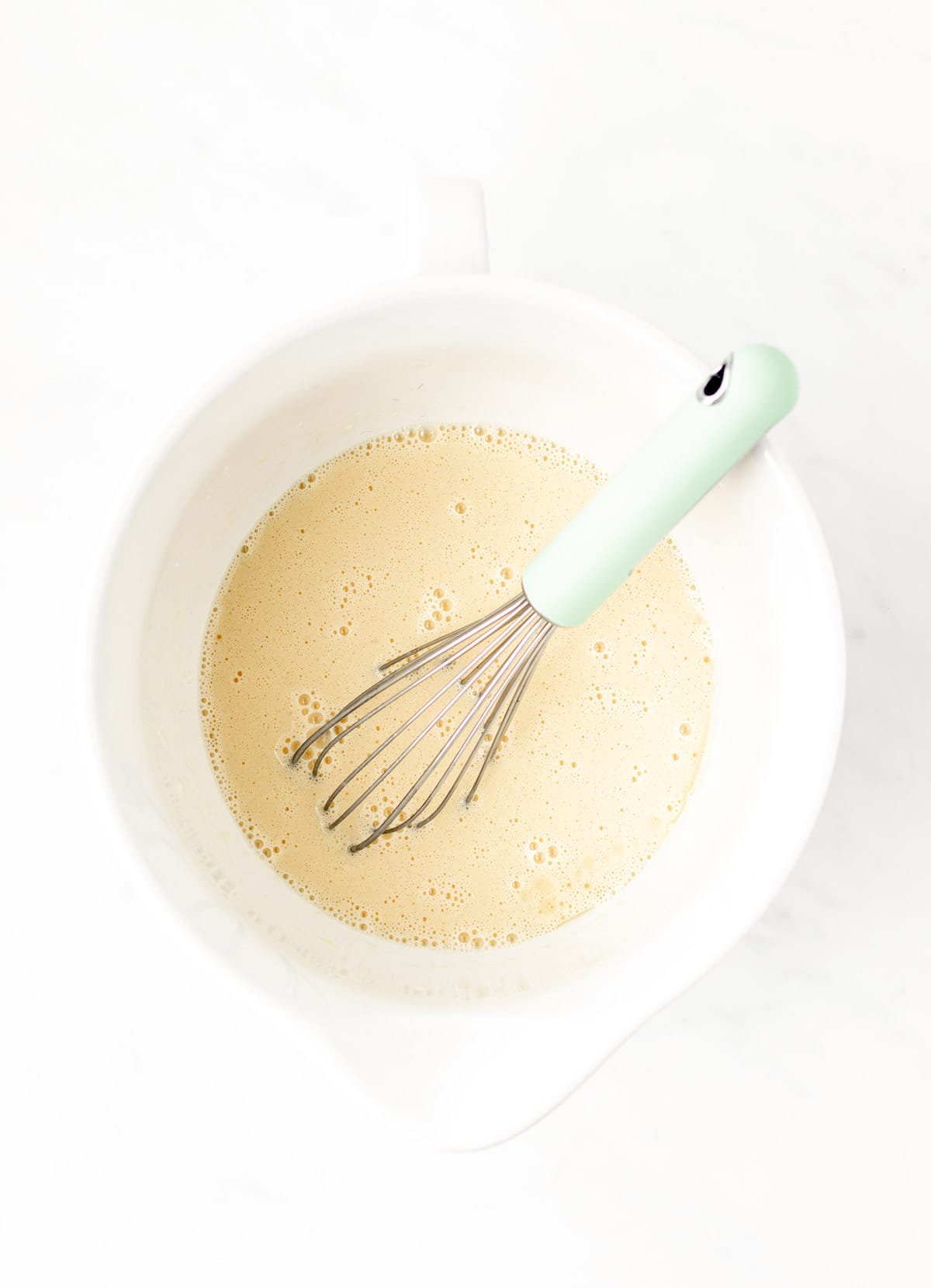A whisk mixing together the wet ingredients for the pancakes in a white bowl.