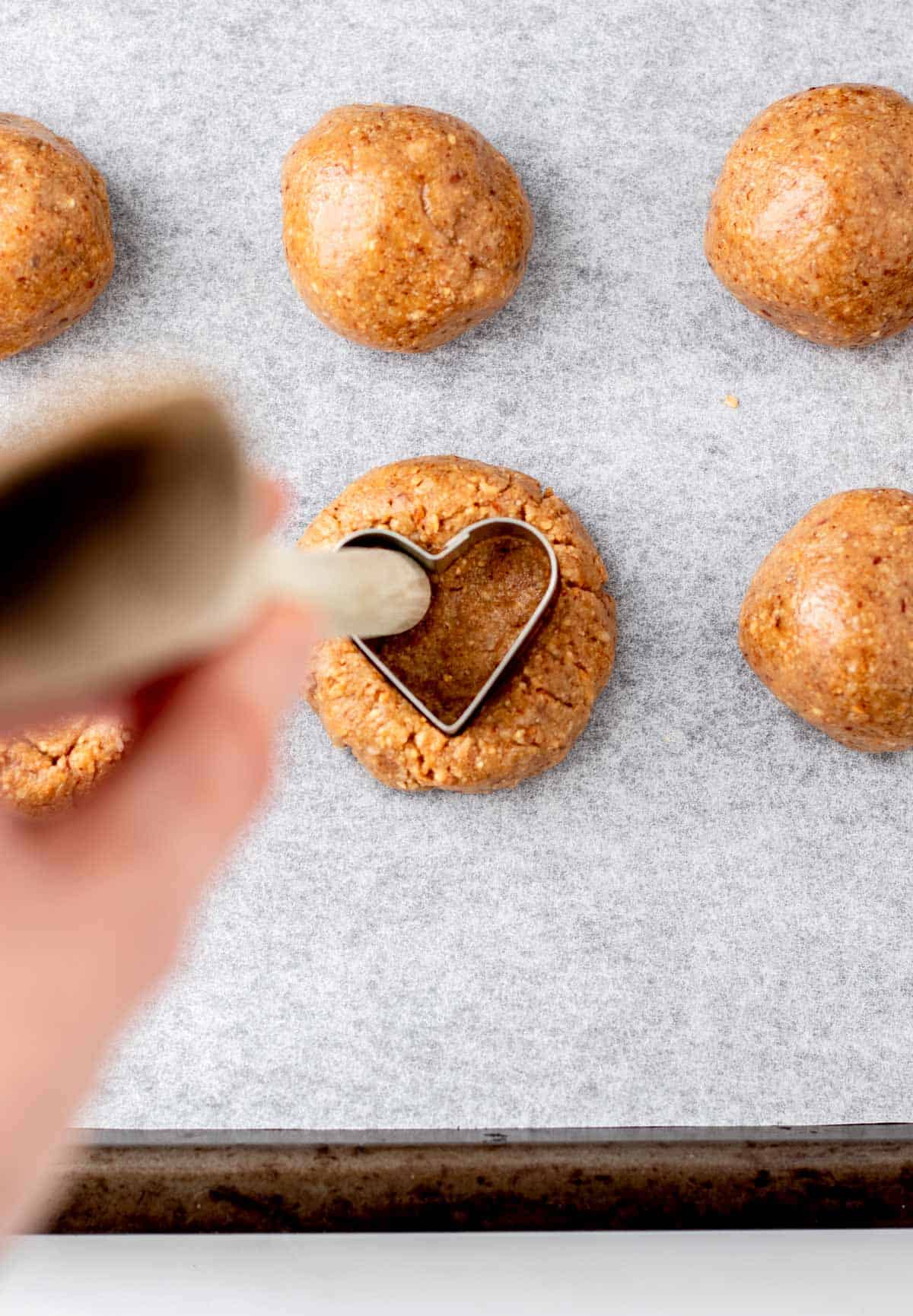 Balls of dough on a cookie sheet with a heart shaped cookie cutter in one of the dough balls.