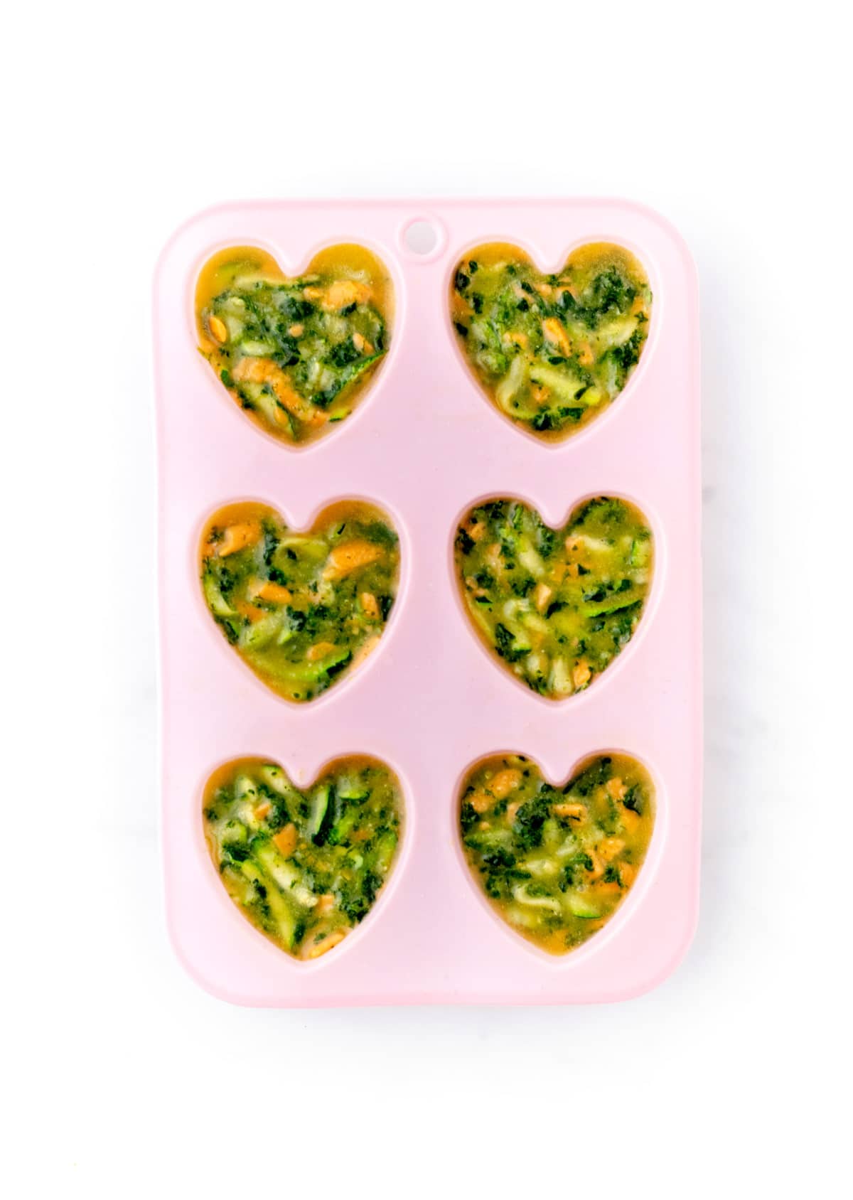 The zucchini frittata muffin mixtures in mini heart-shaped molds.