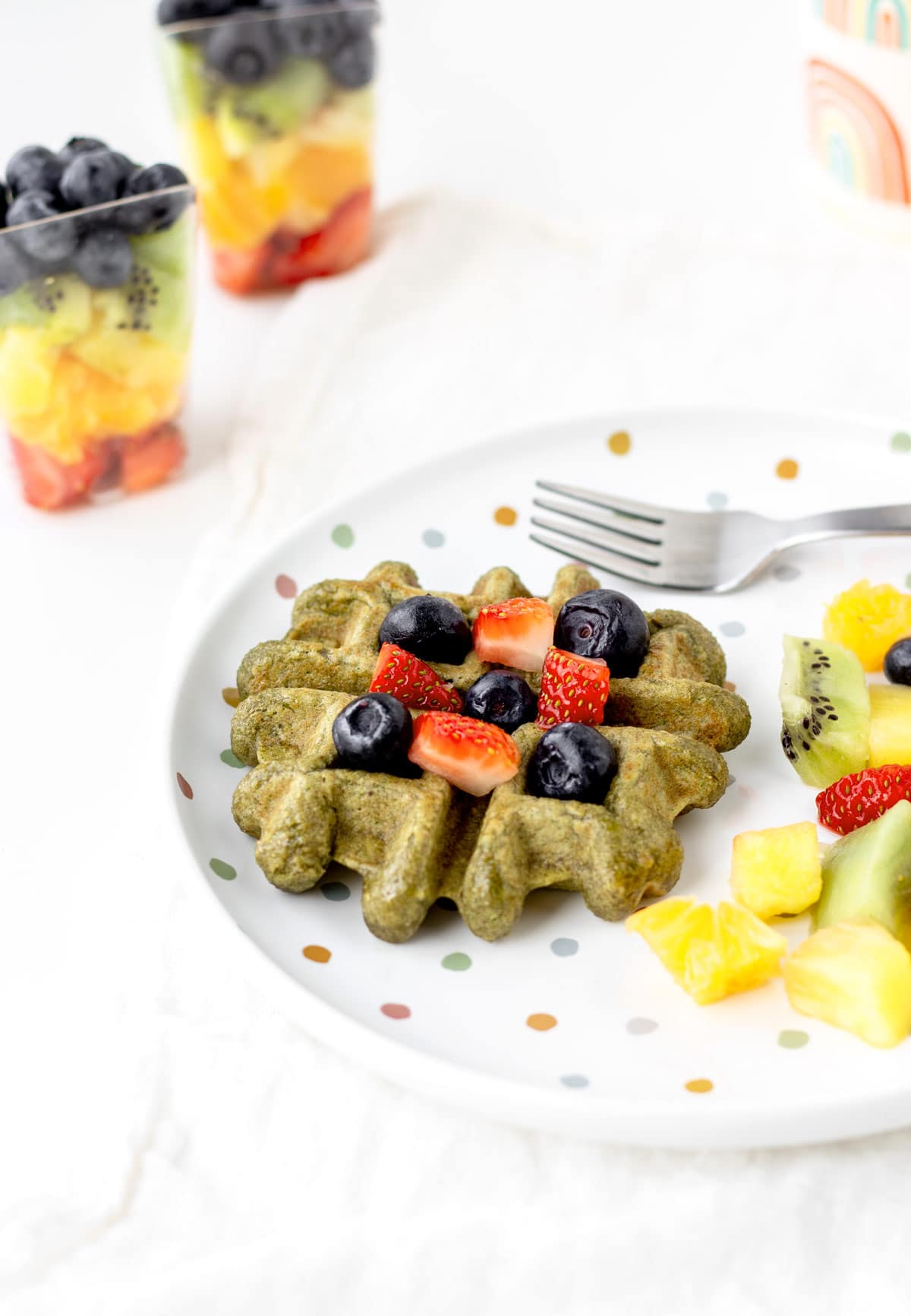 A close-up of the spinach banana waffle topped with berries on a plate next to berries.