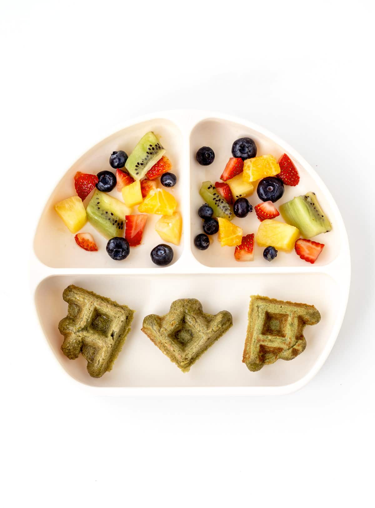 A divided plate with a cut banana spinach waffle and mixed fruit.