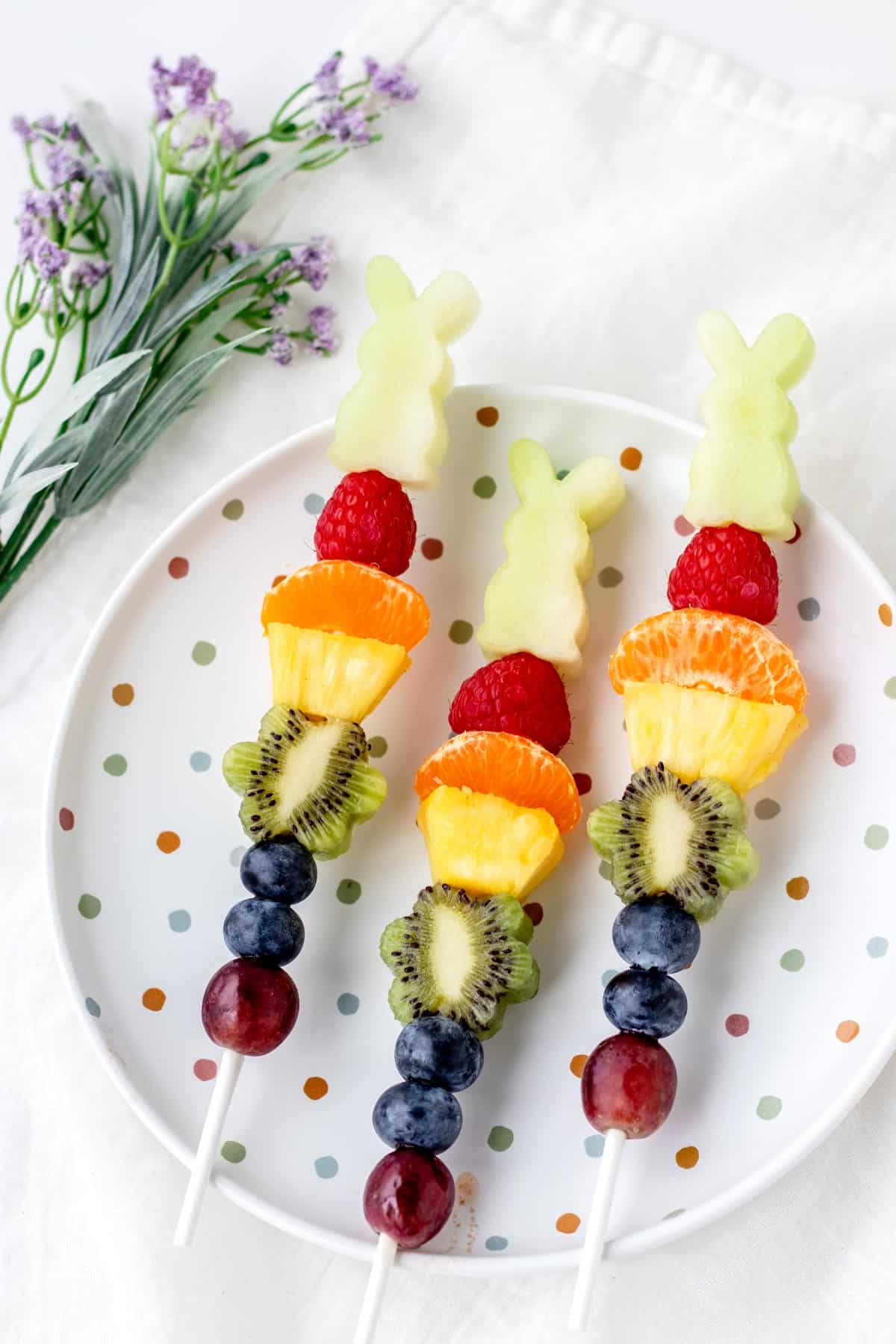 Easter fruit kabobs with bunny-shaped honeydew melon on a polka dotted plate.