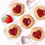 Heart thumbprint cookies on a pink striped plate with a strawberry.