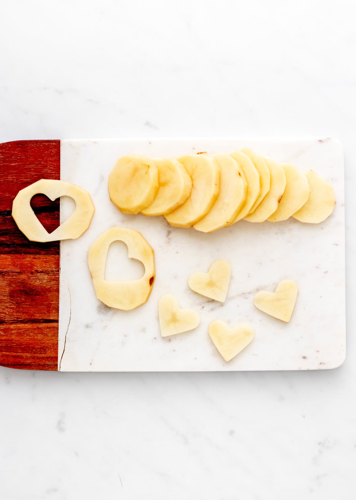 Cutting heart shapes out of the potato slices on a wood cutting board.