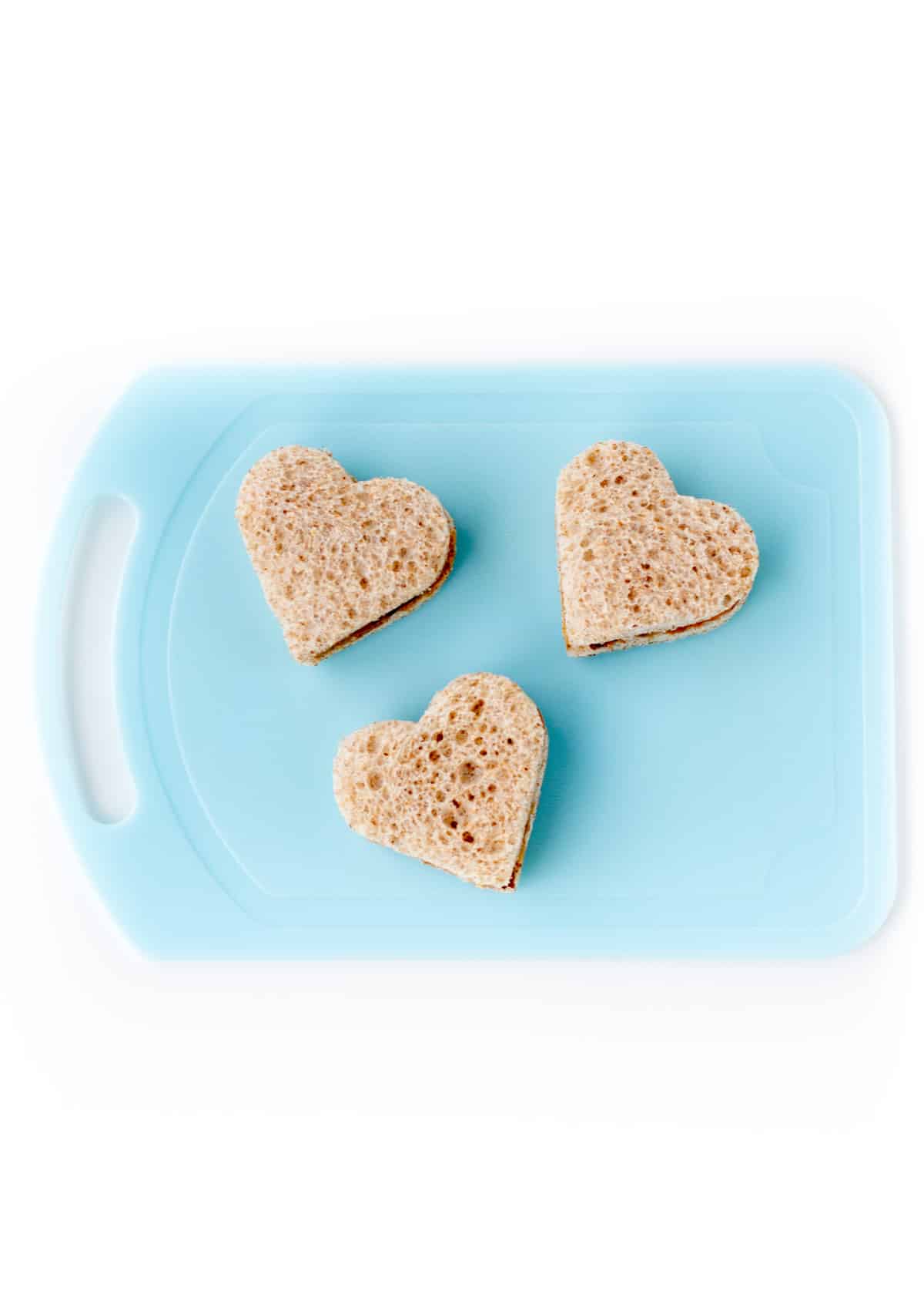 3 heart shaped peanut butter sandwiches on a cutting board.