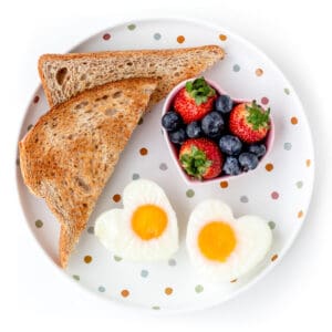 A plate with two egg hearts, two and bowl of berries.