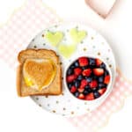Heart egg toast on a plate with berries and honey melon hearts.